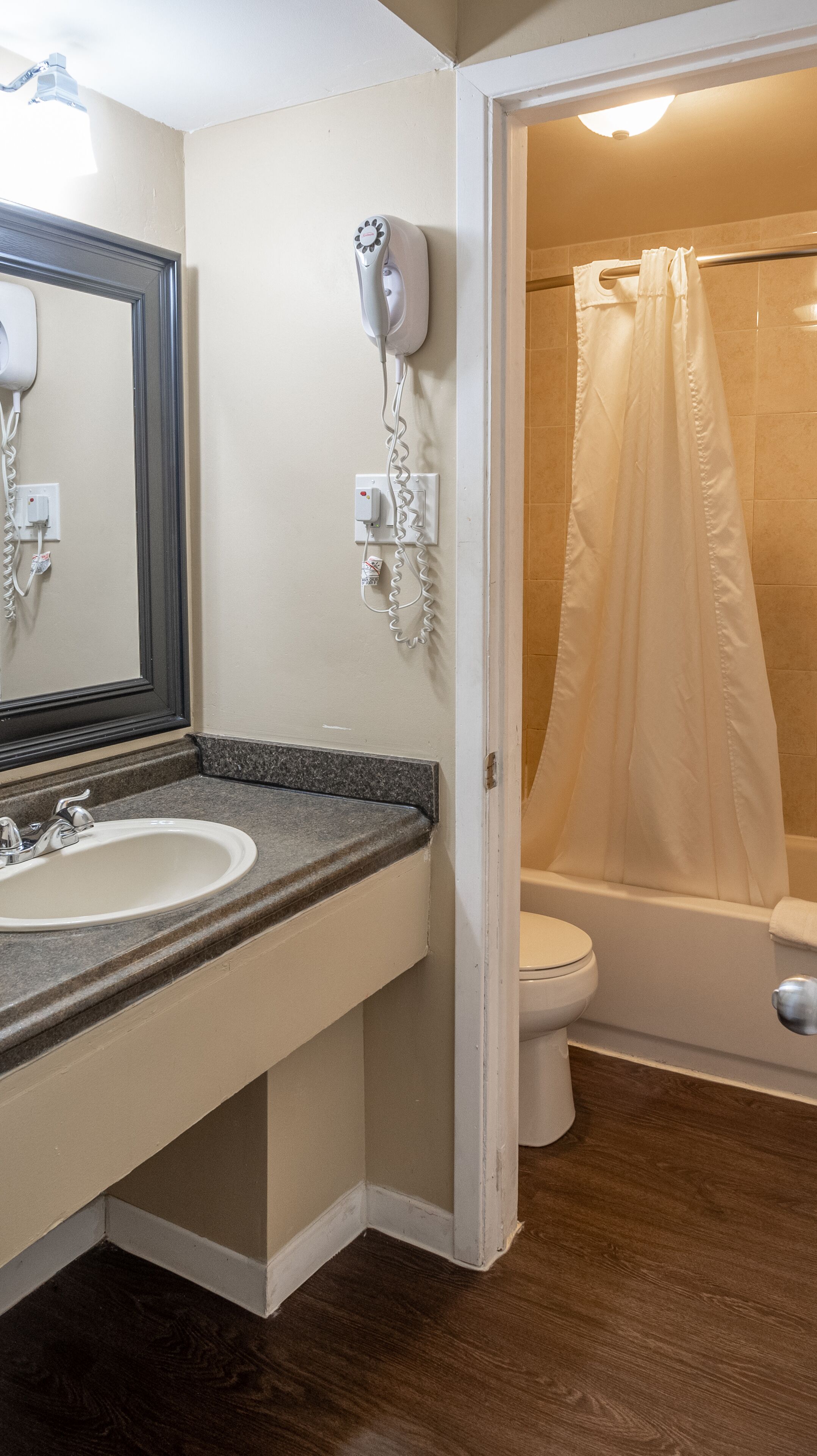 A bathroom with a sink, mirror, hairdryer, and a shower with a curtain.