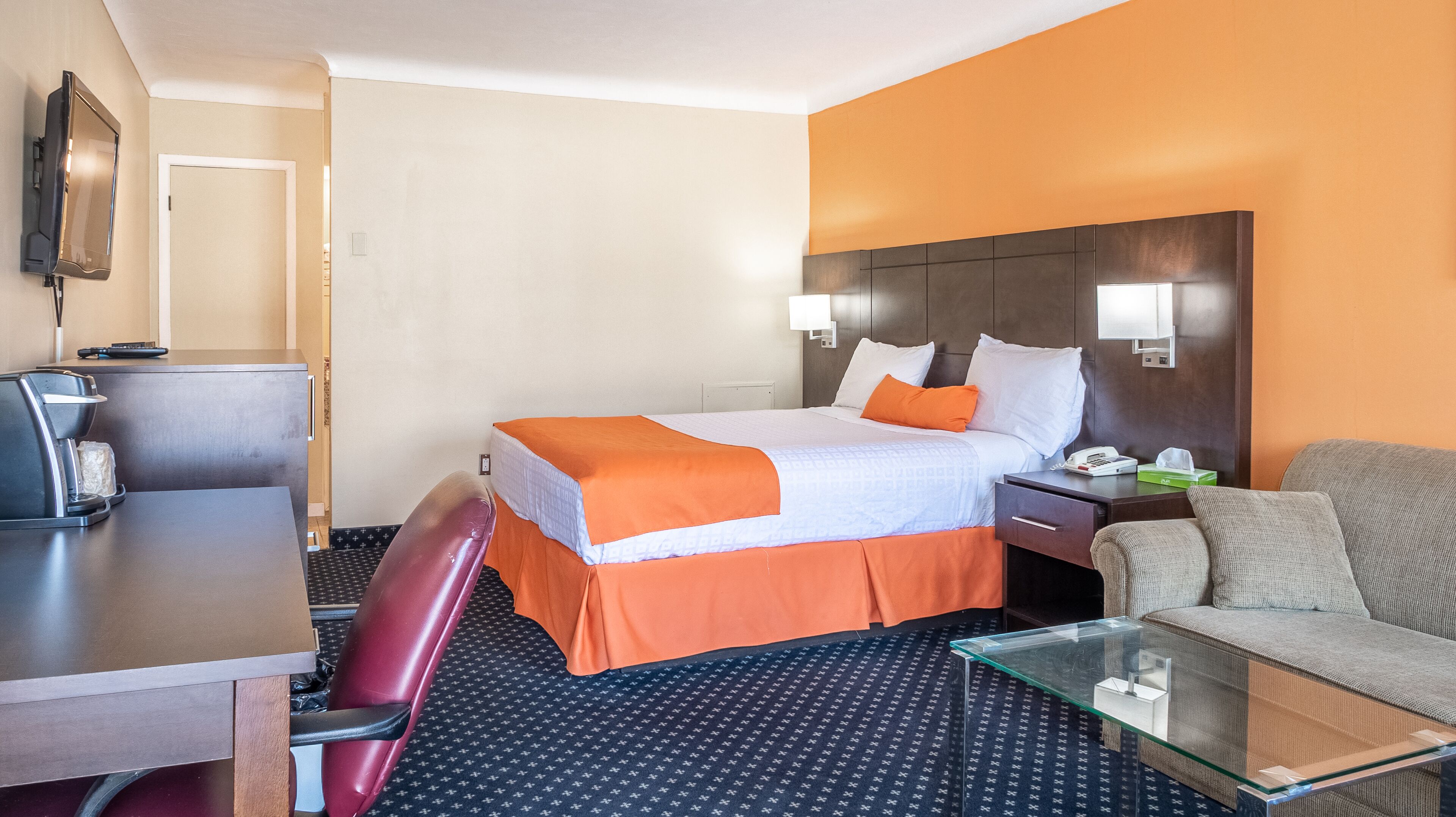 Een hotelkamer met een bed, bureau, stoel, bank en koffieapparaat.