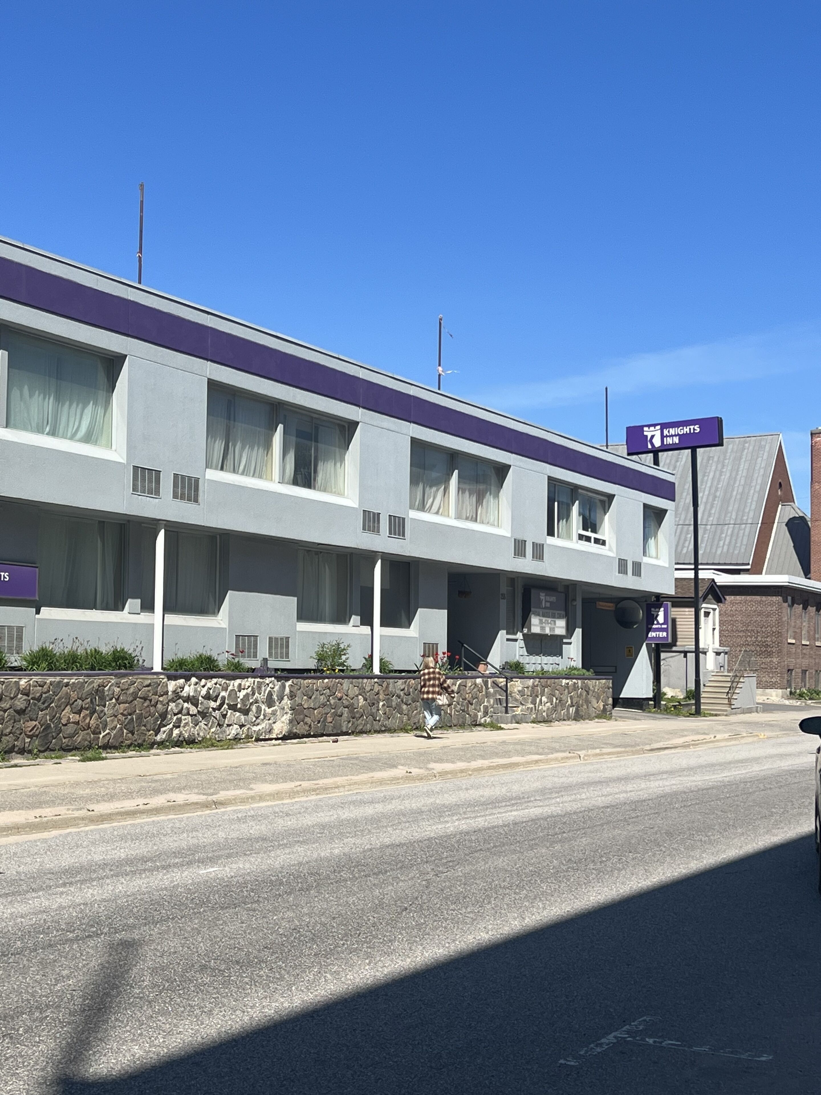 A Knights Inn building with a stone wall and a clear blue sky.