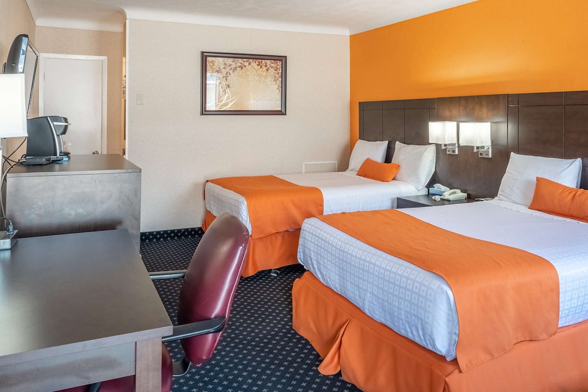 Habitación de hotel con dos camas, un escritorio con computadora, una silla y un cuadro en la pared.