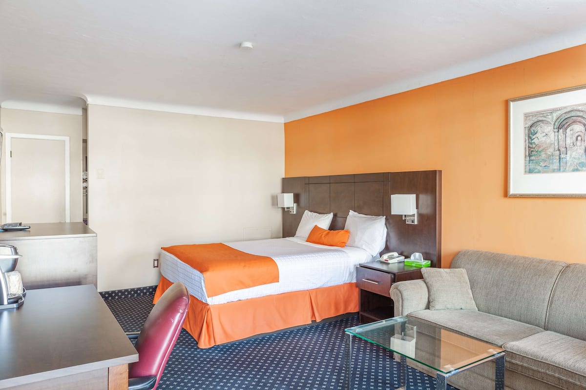 Habitación de hotel con cama, sofá, mesa de centro de vidrio, escritorio y una silla.