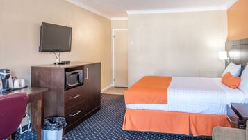 A hotel room with a bed, a desk, a microwave, a television, and a trash can.