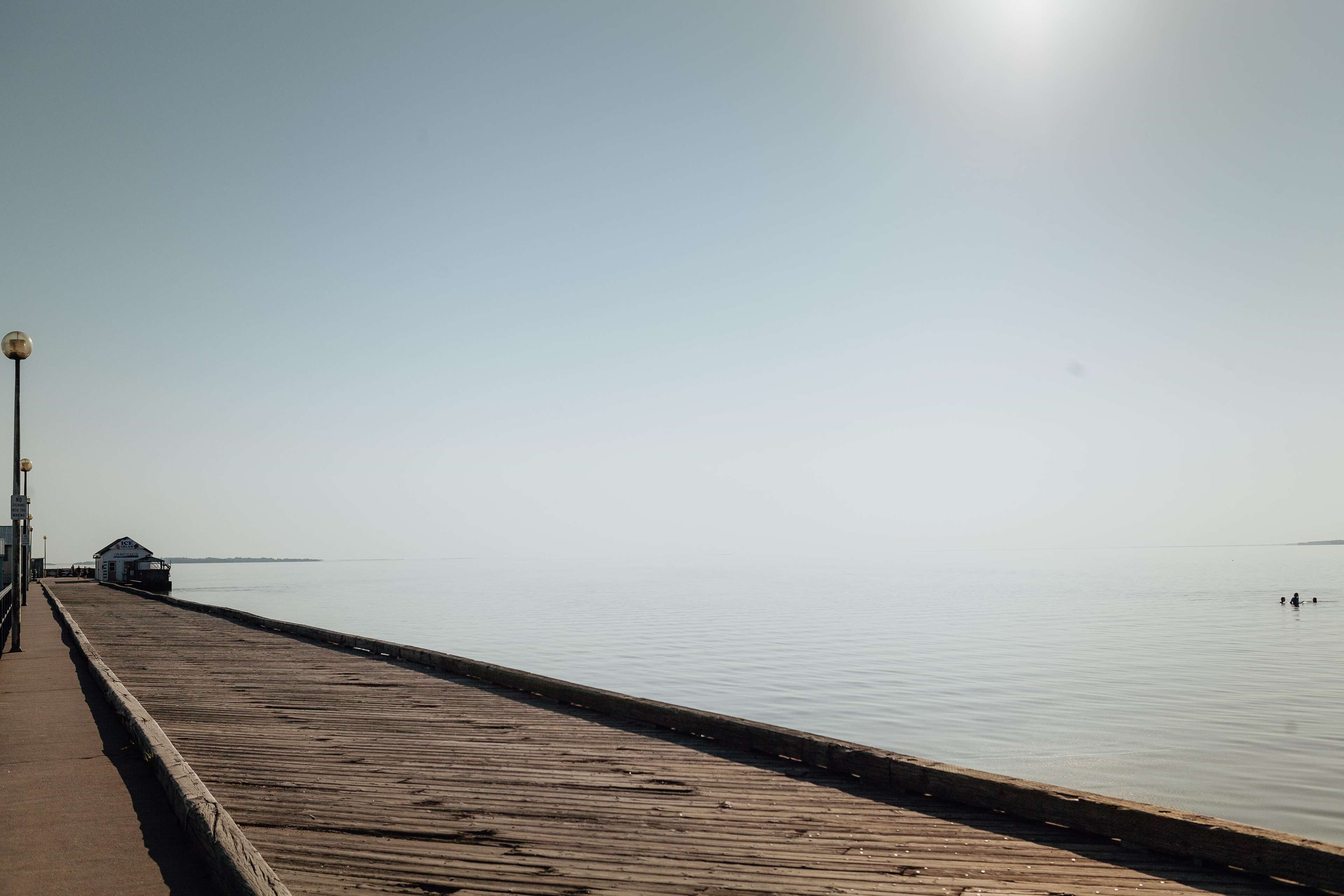 A wooden pier extending into calm water with a clear sky above.