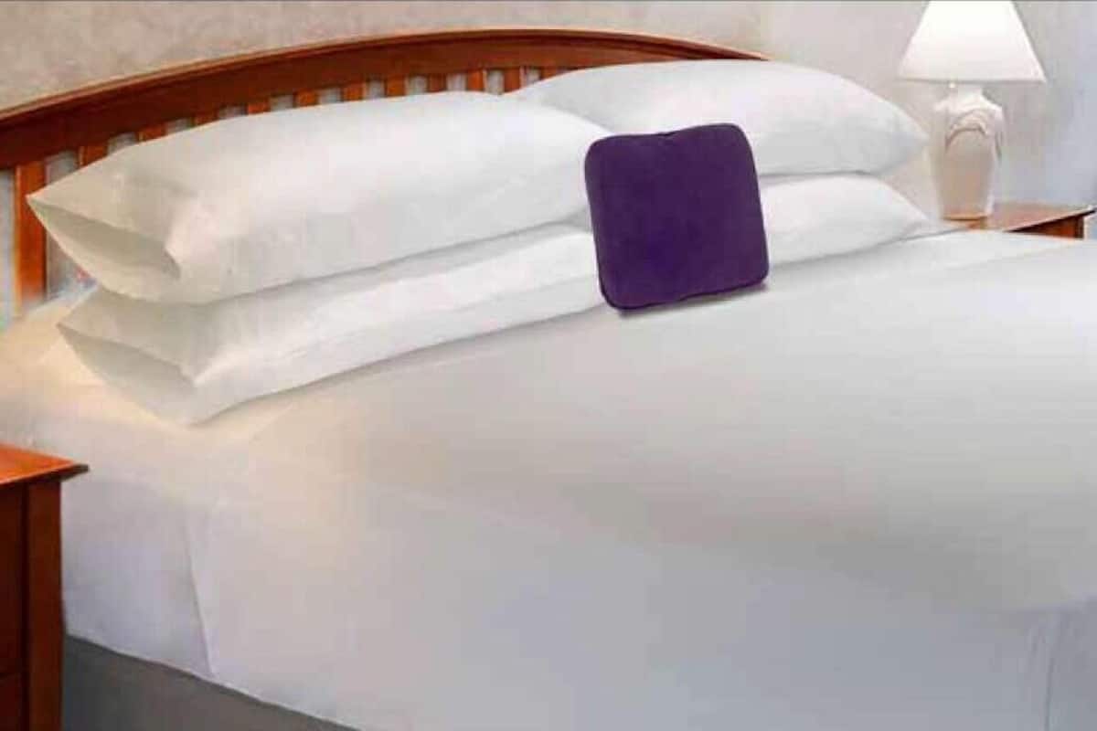 Una cama con sábanas blancas y una almohada morada.