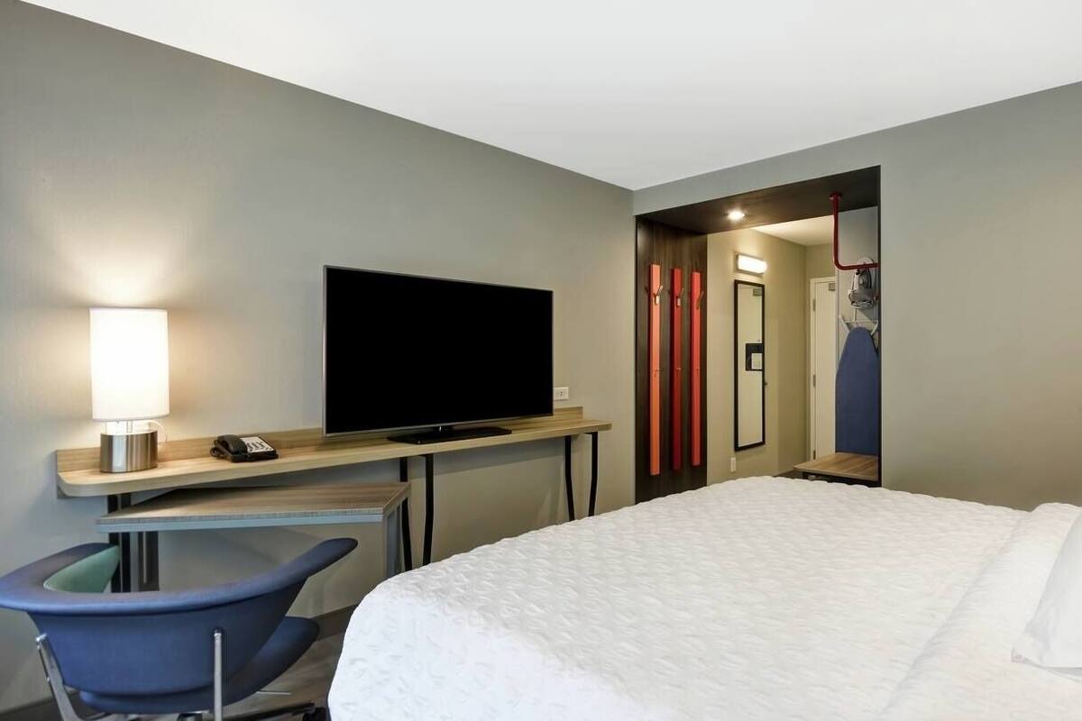 Habitación de hotel con cama, escritorio con televisor, silla y baño visible a través de una puerta abierta.