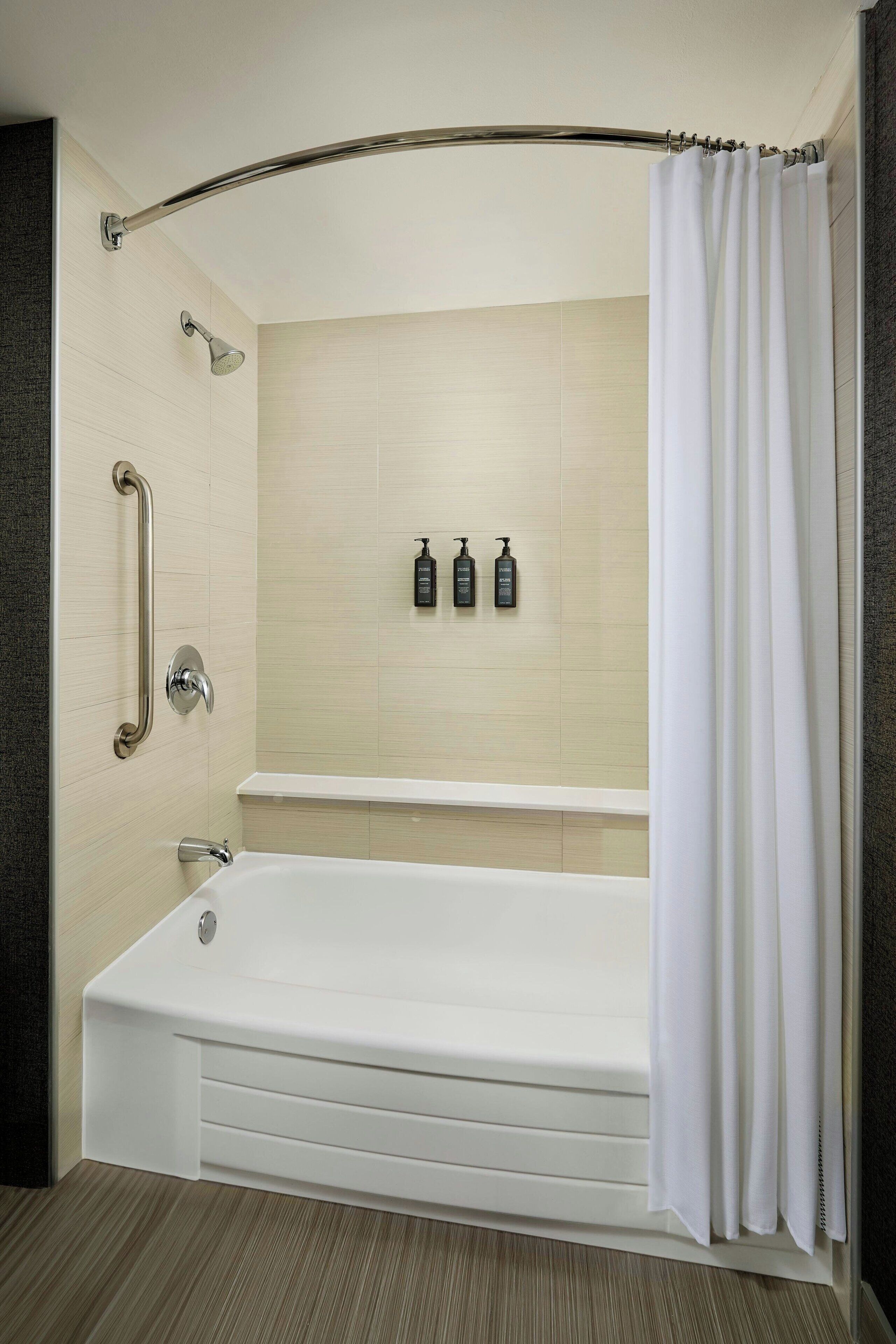 A modern bathroom with a bathtub, a shower, and a handrail.