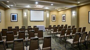 A conference room with rows of chairs, a projector screen, and framed pictures on the walls.