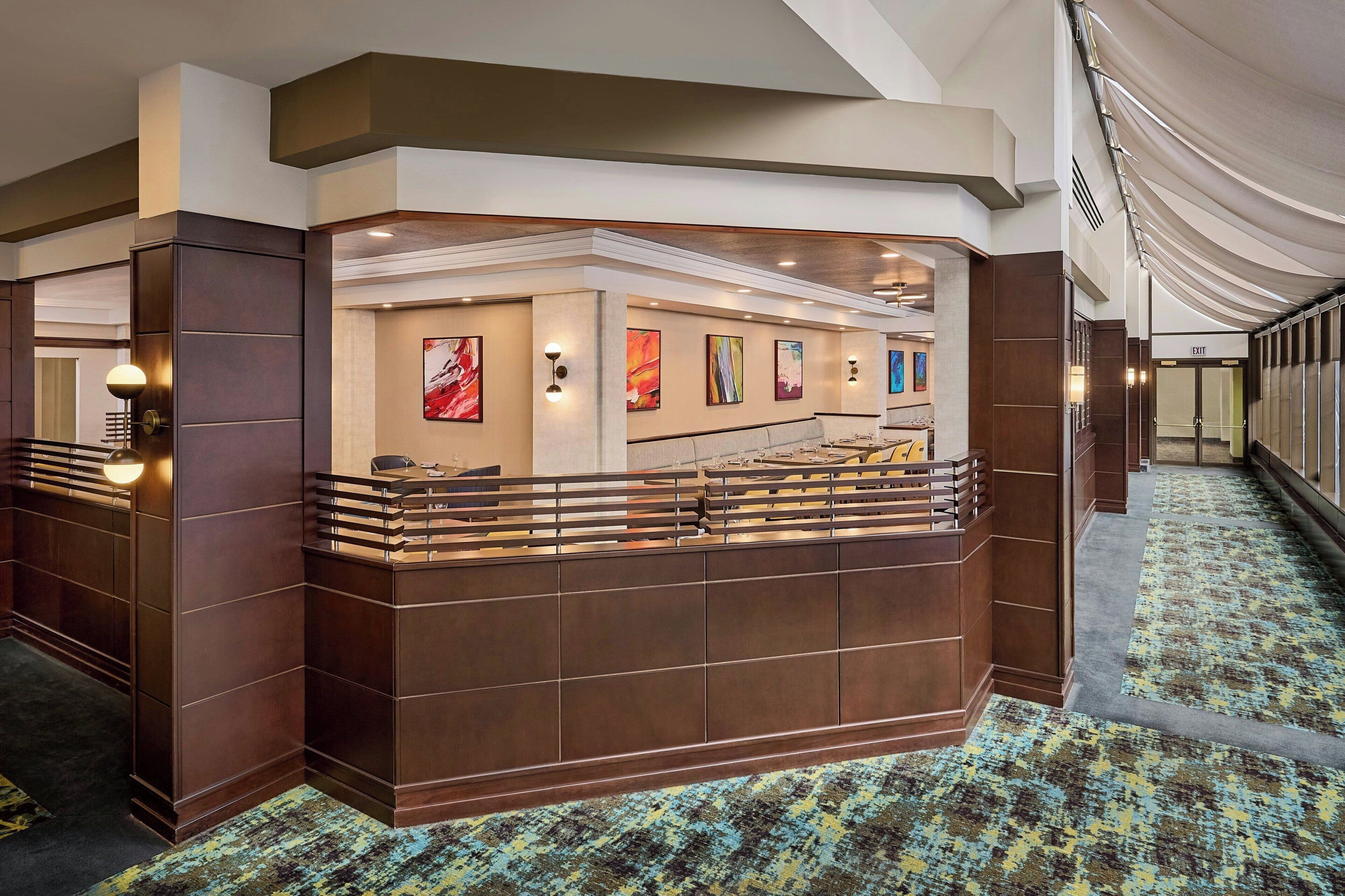 Et hotellets reception område med moderne design, med en receptionsdisk, kunst på væggene og et mønstret tæppe.