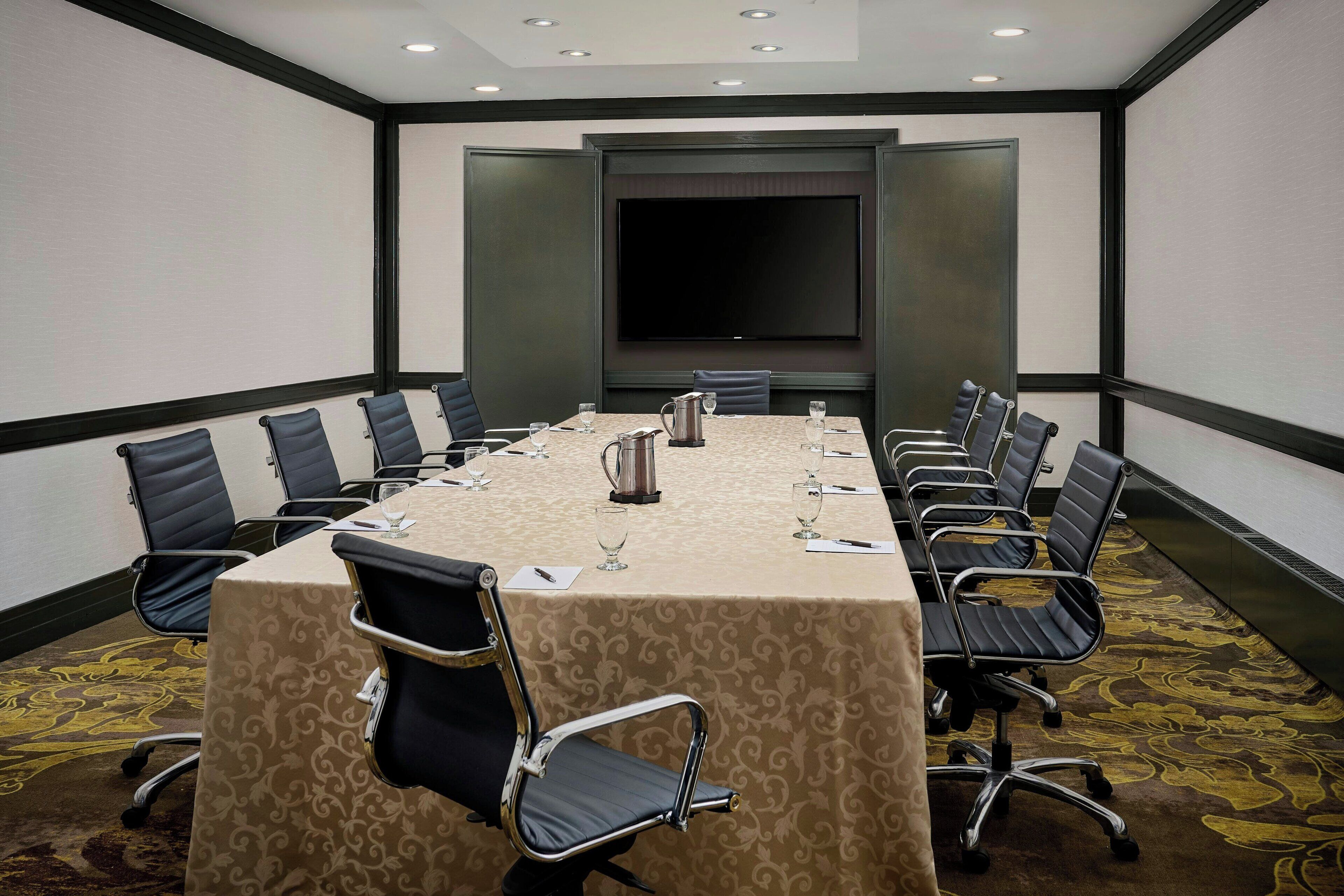 A conference room with a long table, black chairs, a large screen, and a carpeted floor.