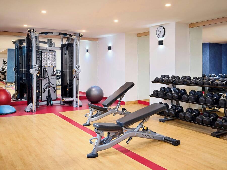 Uma academia com equipamentos de ginástica, um banco e uma estante com halteres.