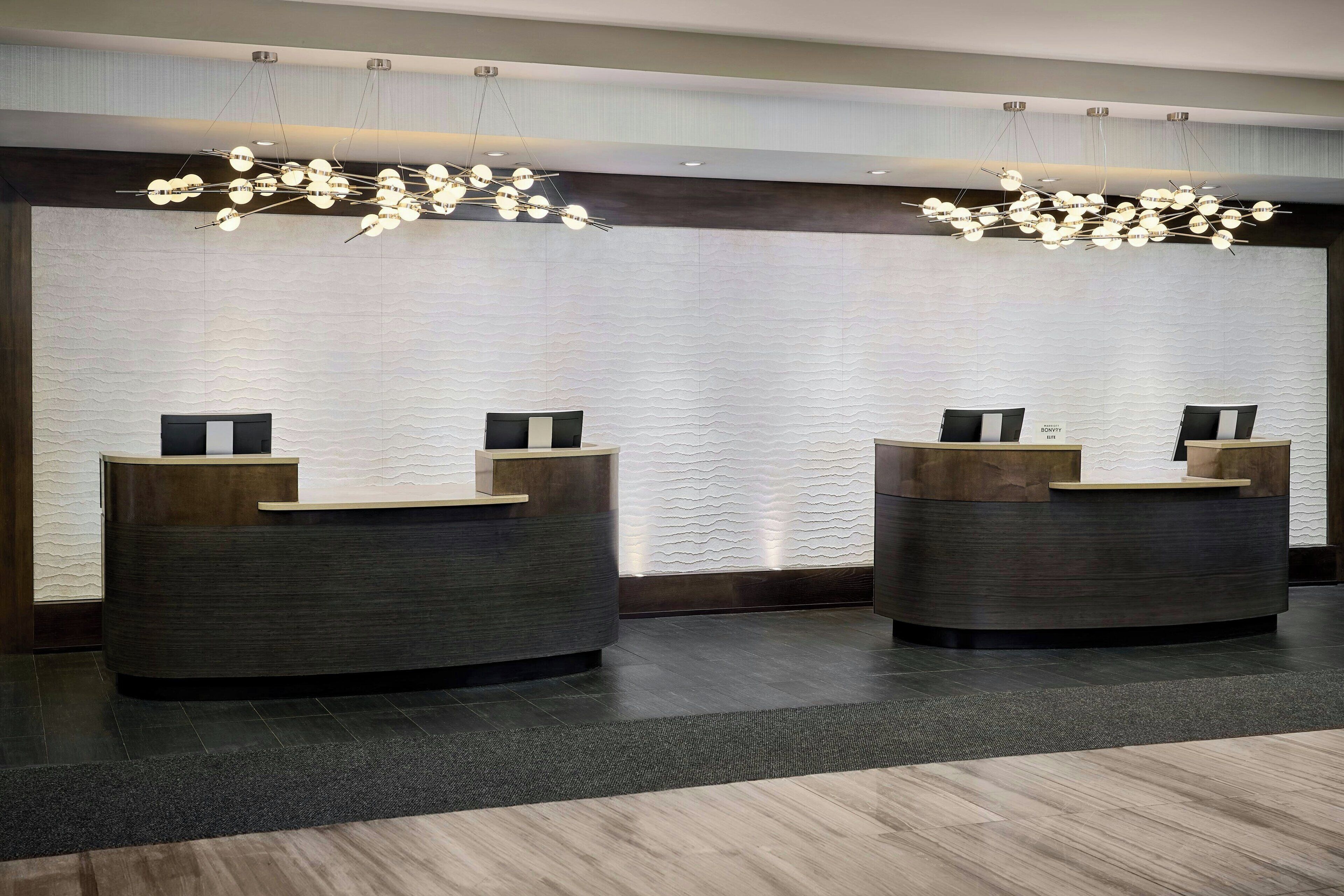 A reception area with two curved reception desks, a textured wall, and a modern chandelier.