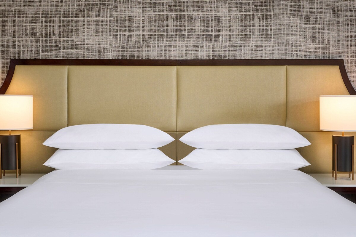 A neatly made bed with a headboard, two bedside lamps, and a textured wall behind.