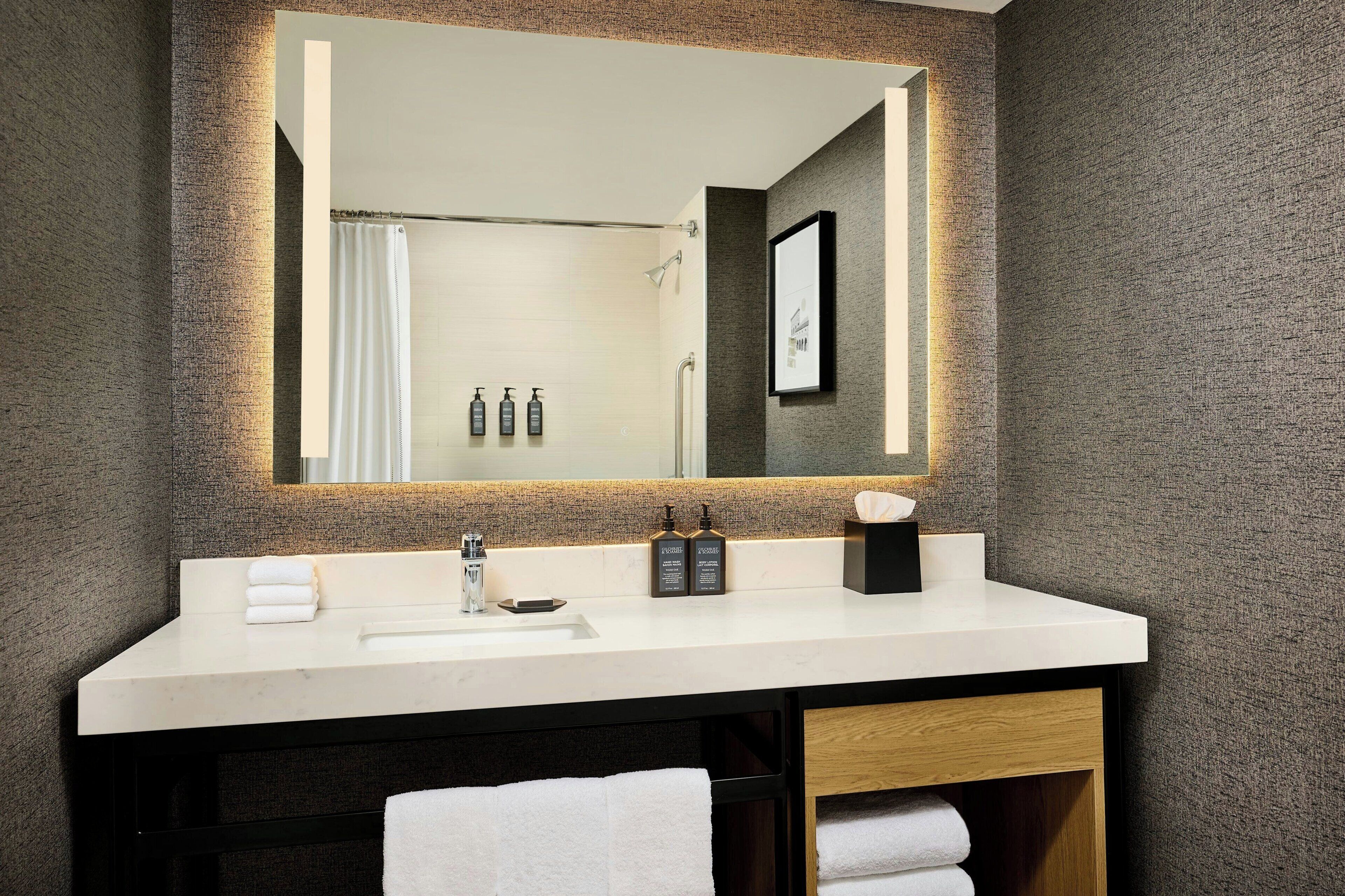 A modern bathroom with a large mirror, white sink, and towel storage.
