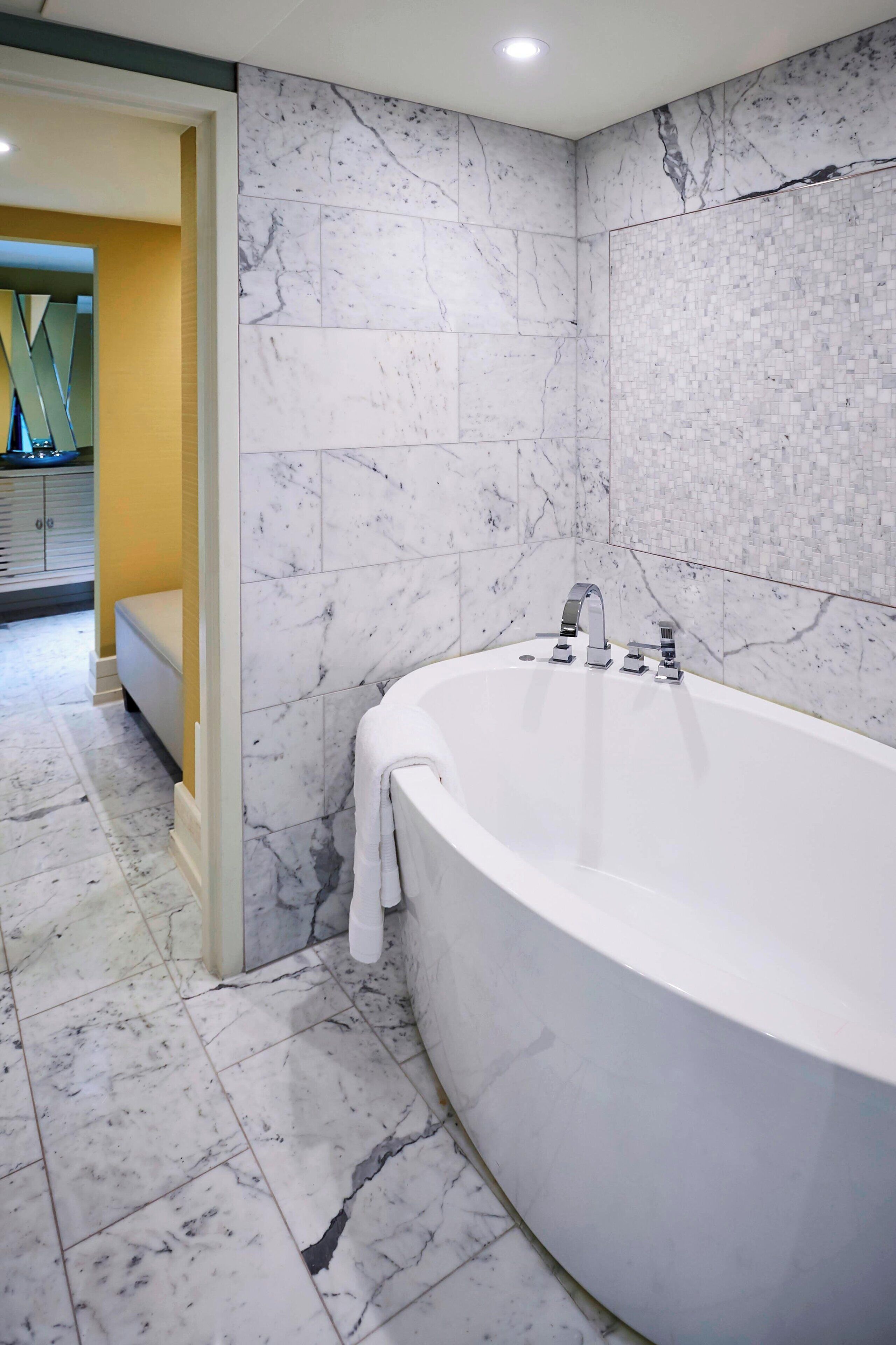 A modern bathroom with a freestanding bathtub, marble walls, and a yellow accent wall.