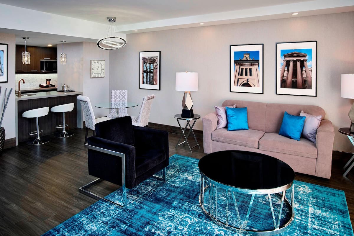 A modern living room with a sofa, a black chair, a coffee table, and a kitchen area in the background.