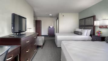 Ein Hotelzimmer mit zwei Betten, einem Schreibtisch mit Fernseher, einem Schminktisch, einer kleinen Kommode und einem Nachttisch mit Lampe.