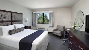 Habitación de hotel con una cama grande, un escritorio, una silla, un aparador y un ventanal con cortinas.
