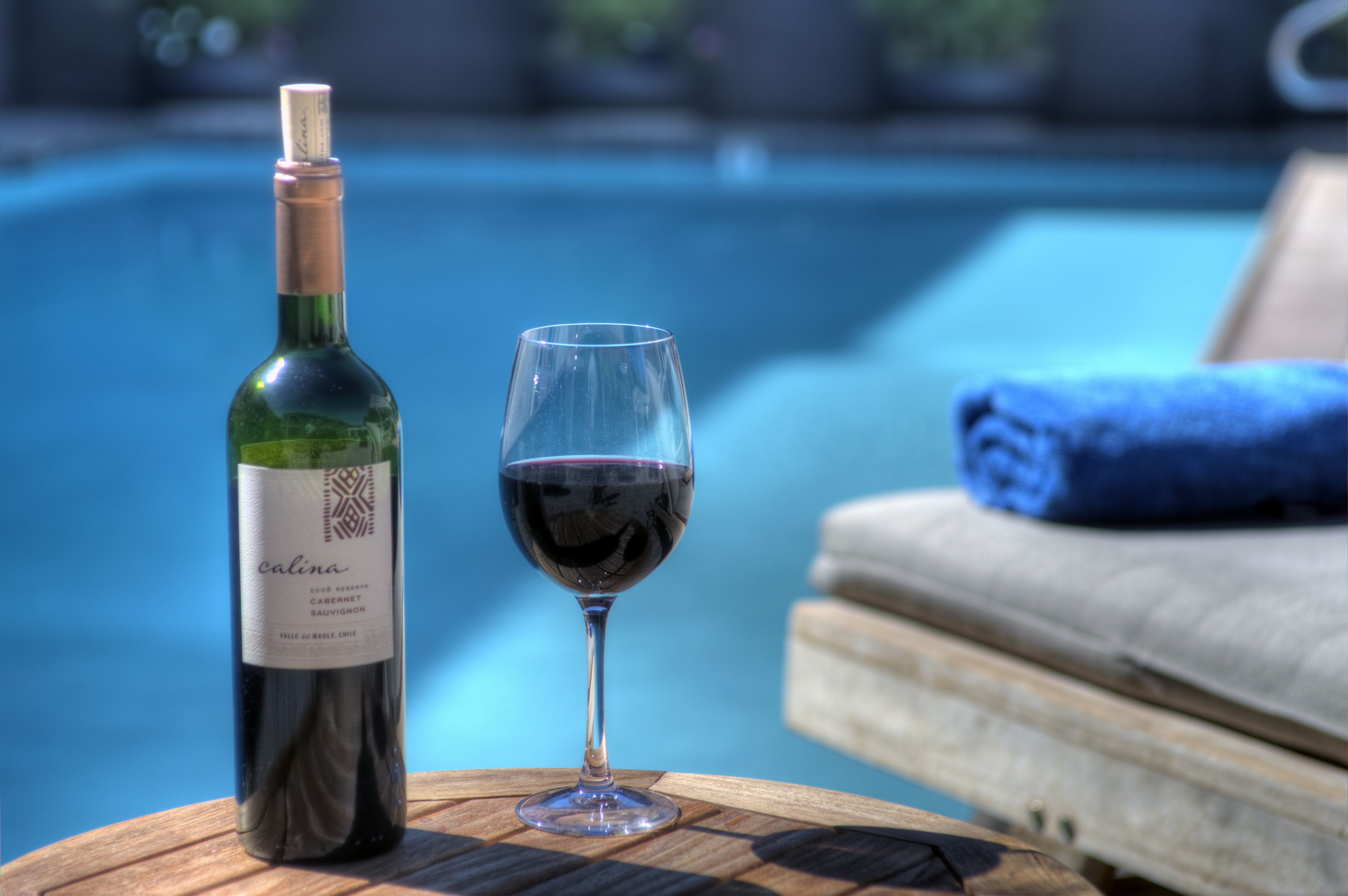 Eine Weinflasche und ein Weinglas auf einem Holztisch am Pool.