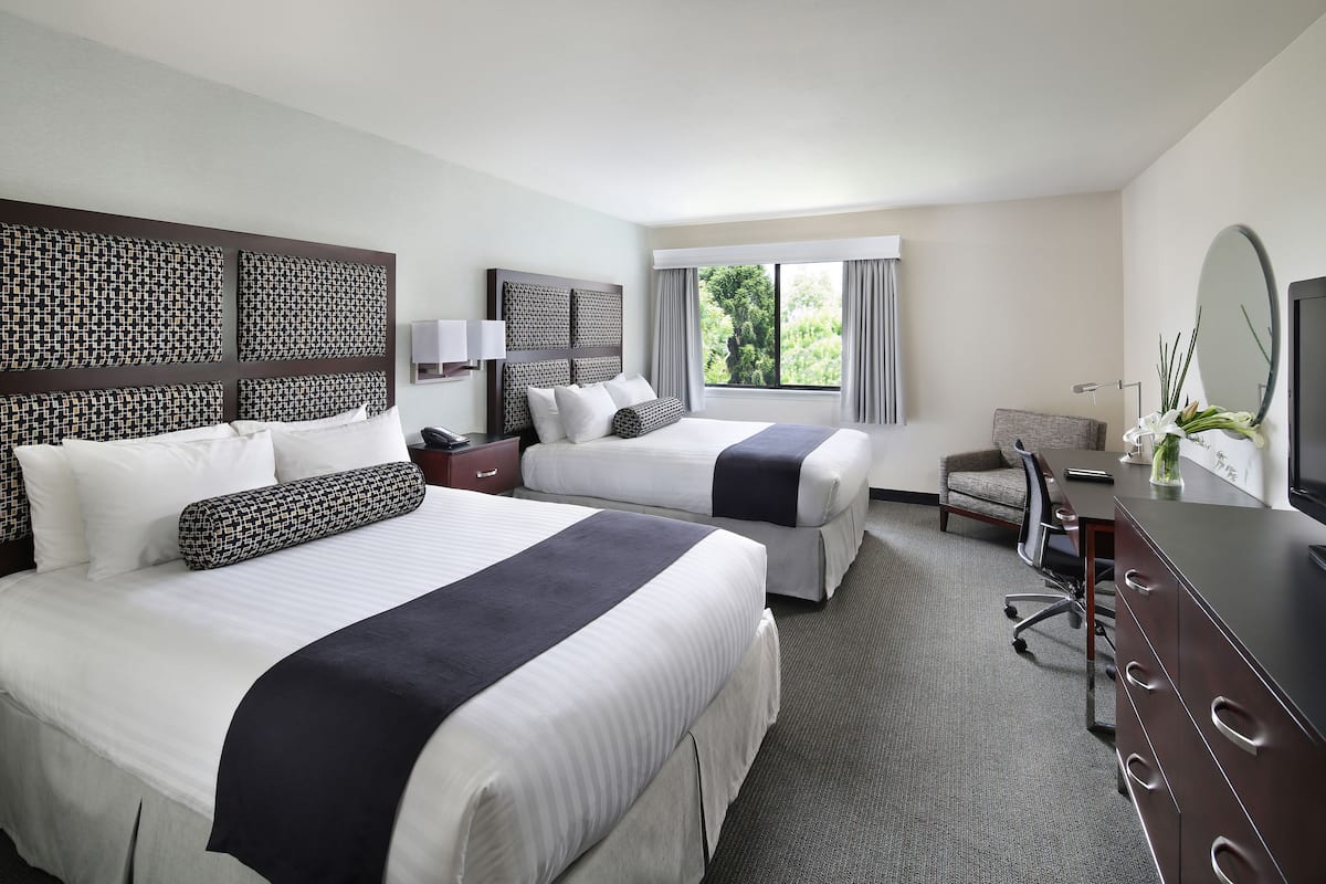 A hotel room with two beds, a desk, a chair, and a large window.