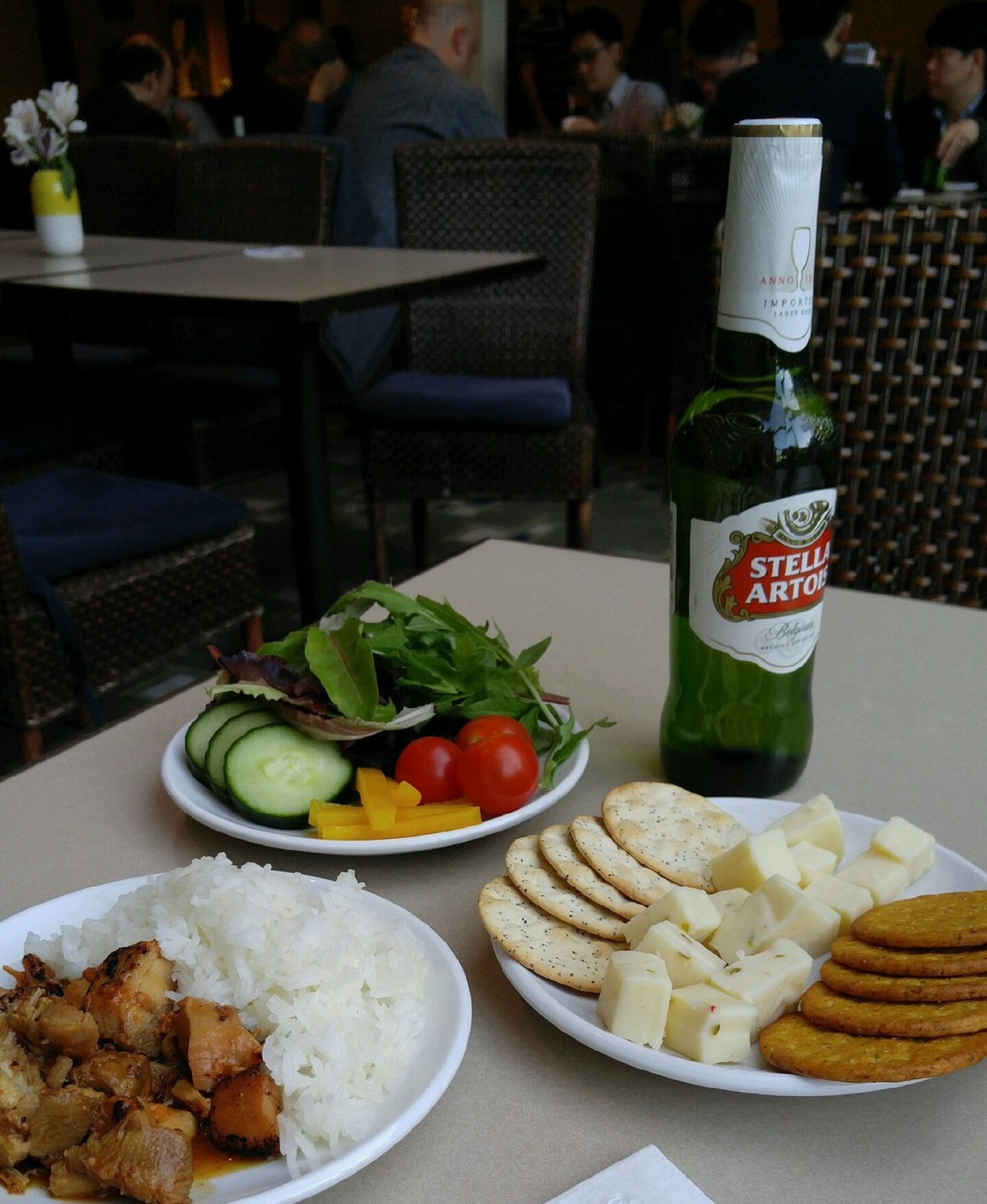 A table with plates of food, including rice, chicken, cheese, crackers, and a salad. A bottle of Stella Artois beer is also visible.