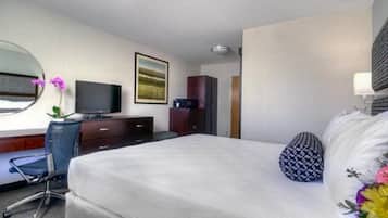 A hotel room with a bed, a desk with a chair, a television, a wardrobe, and a painting on the wall.