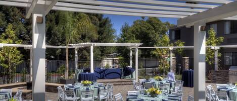 An outdoor patio with tables and chairs, a pergola, and a barbecue area.