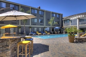 A hotel with a swimming pool, lounge chairs, and umbrellas.