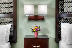 A hotel room with a bed, a nightstand with a vase of flowers, and two wall-mounted lamps.