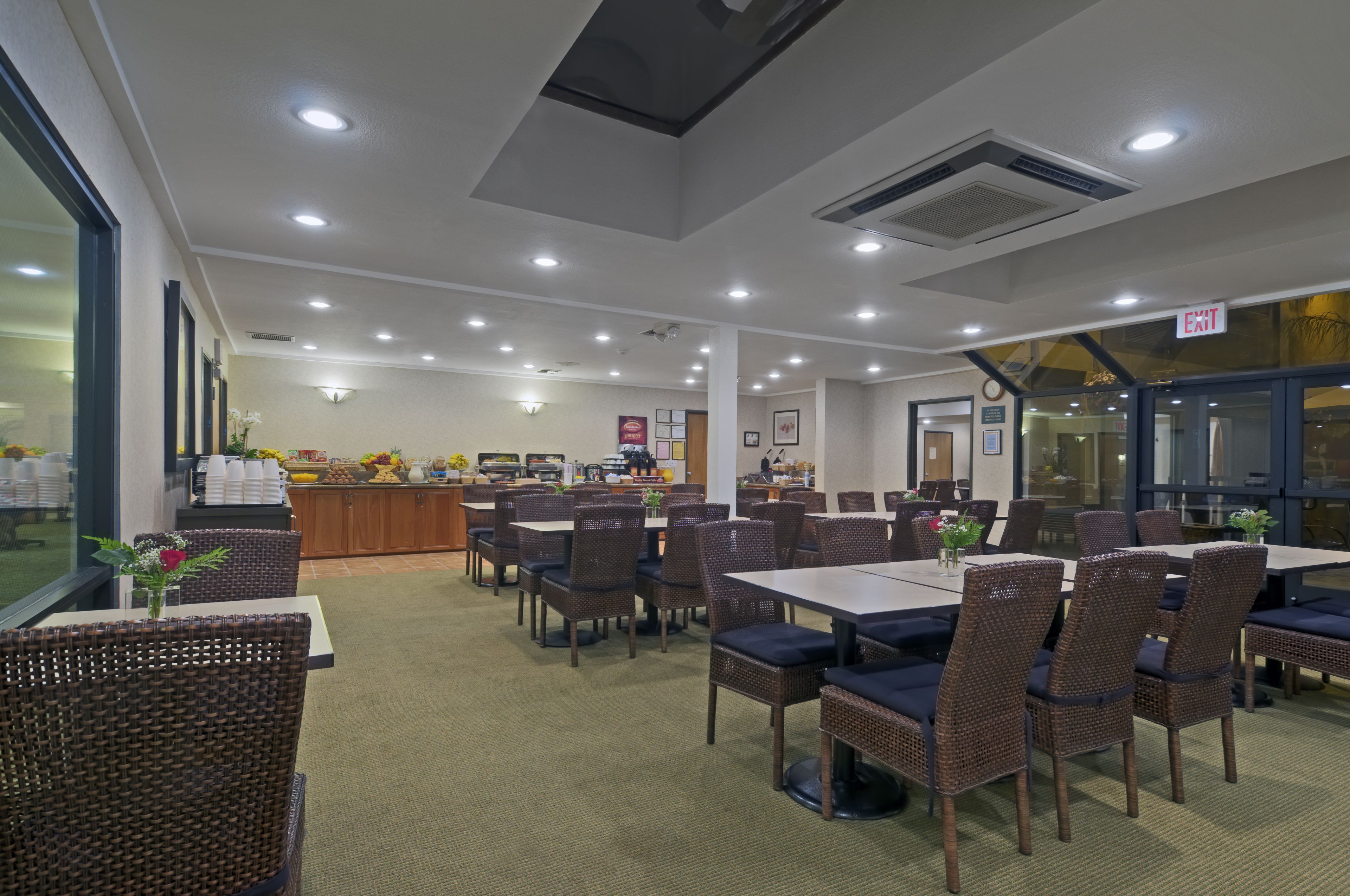 A restaurant with wicker chairs and tables, a kitchen area, and an exit sign.