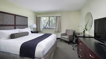 Una habitación de hotel con cama, escritorio con televisor, silla y ventana con cortinas.