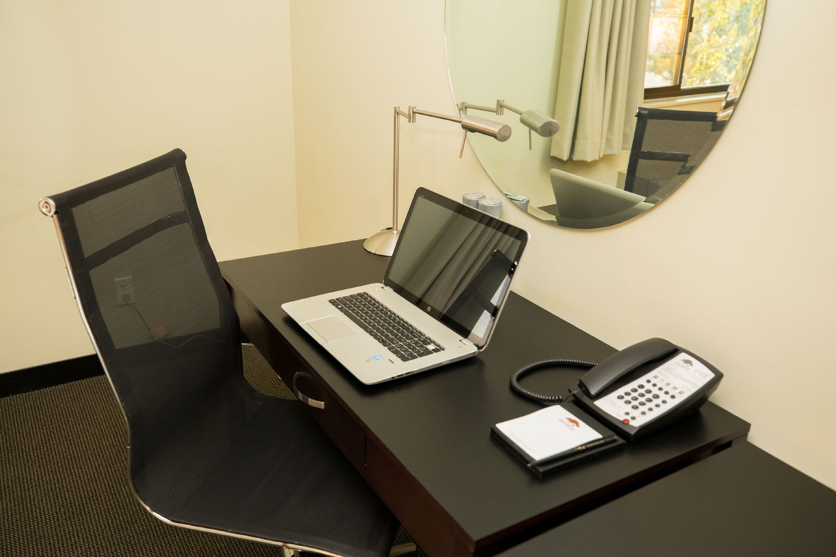 A hotel room with a desk, a laptop, a telephone, and a chair.