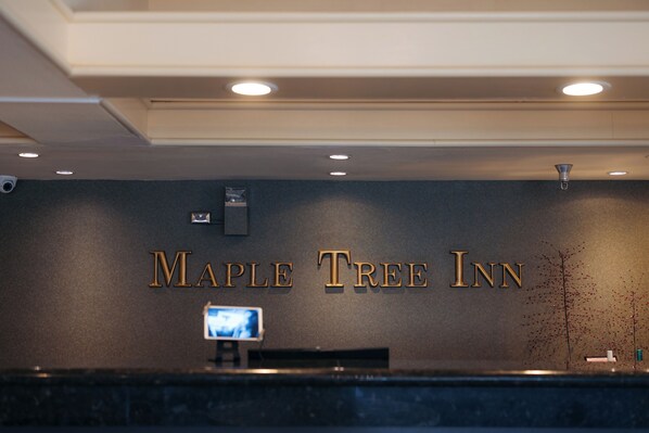 A reception desk with the name 'Maple Tree Inn' in gold lettering on the wall. - Maple Tree Inn (Sunnyvale)