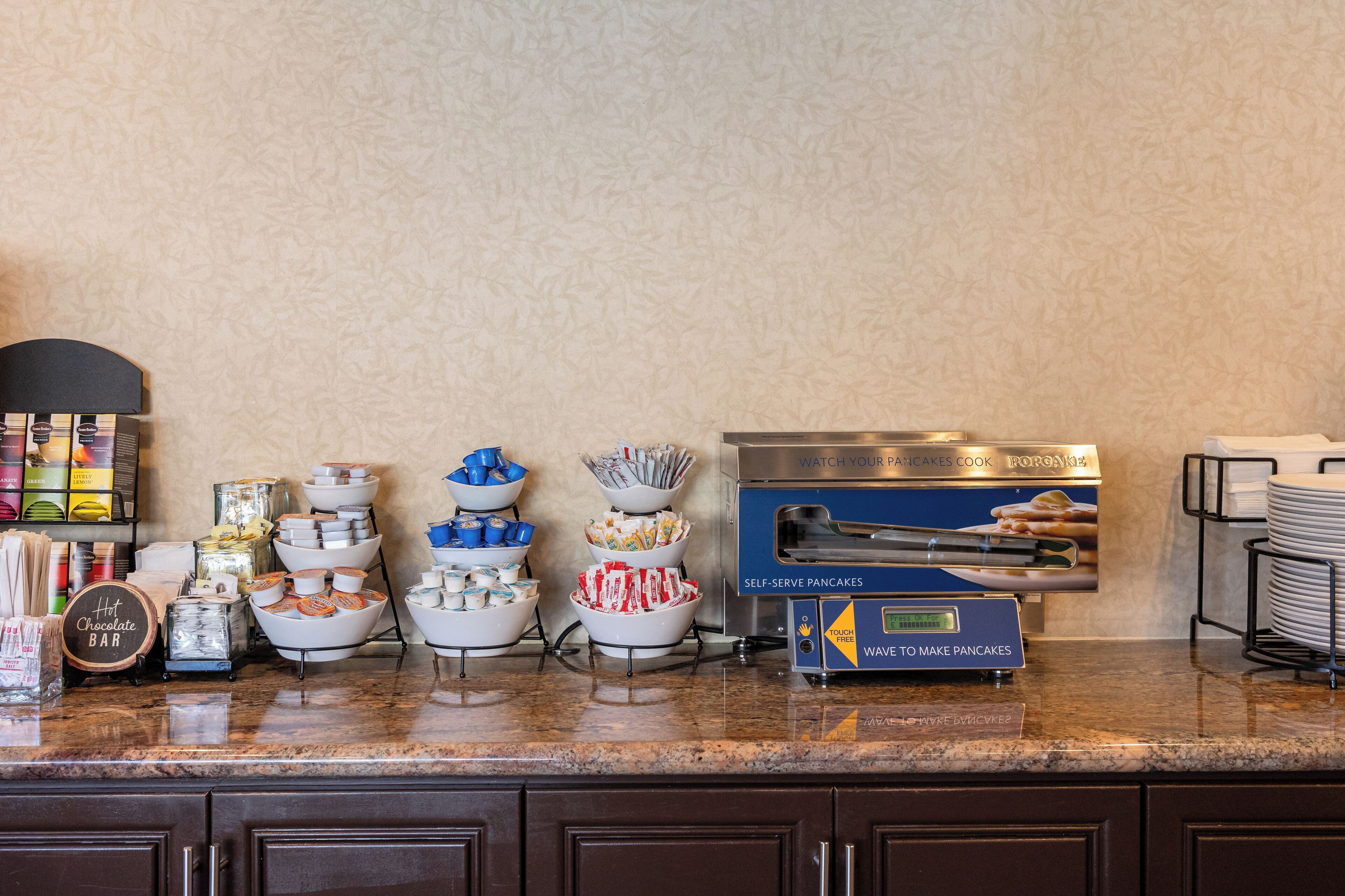 A breakfast buffet setup with various food items and a self-serve pancake machine.