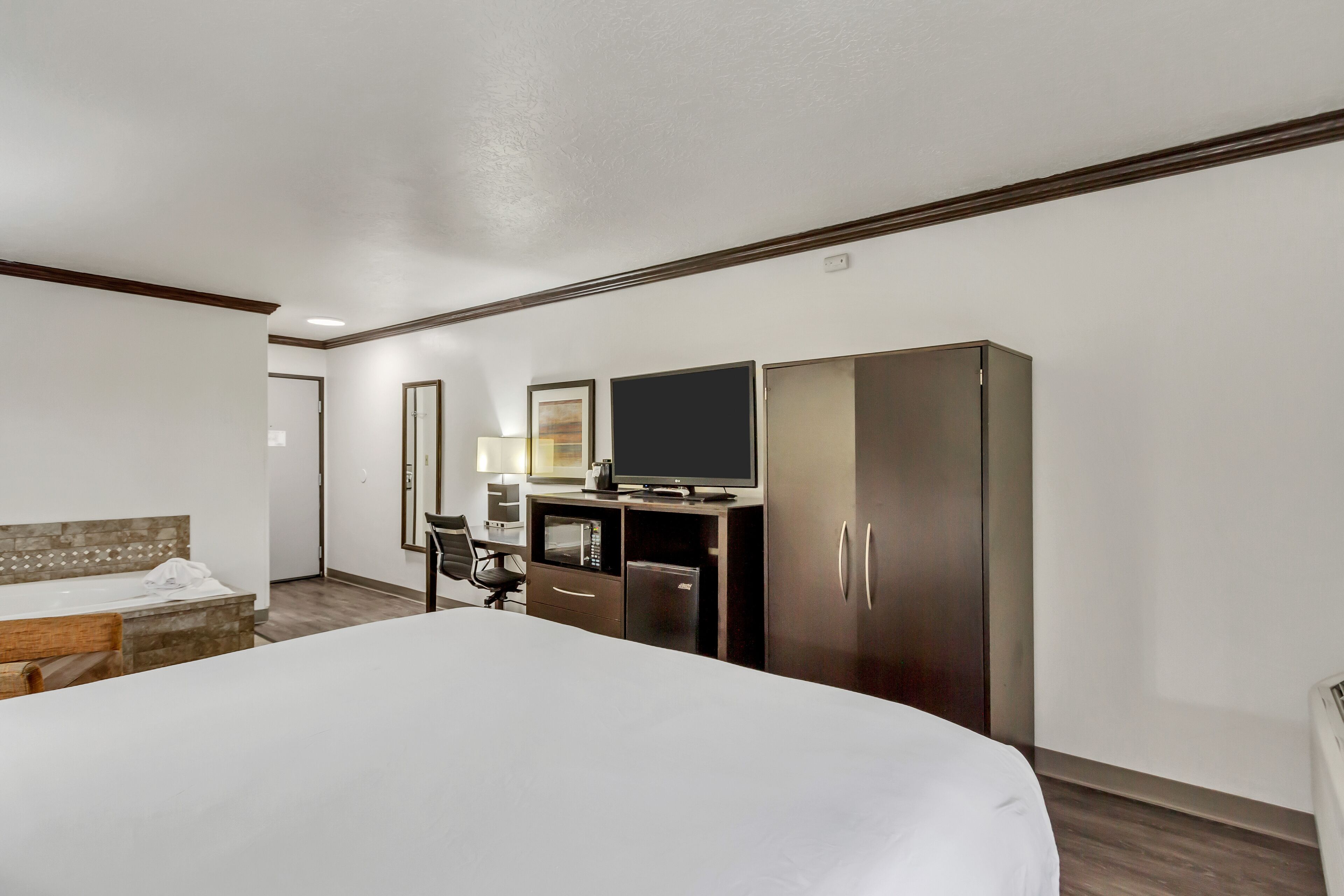 Une chambre d’hôtel avec un grand lit, un bureau avec un ordinateur, une télévision et une armoire.