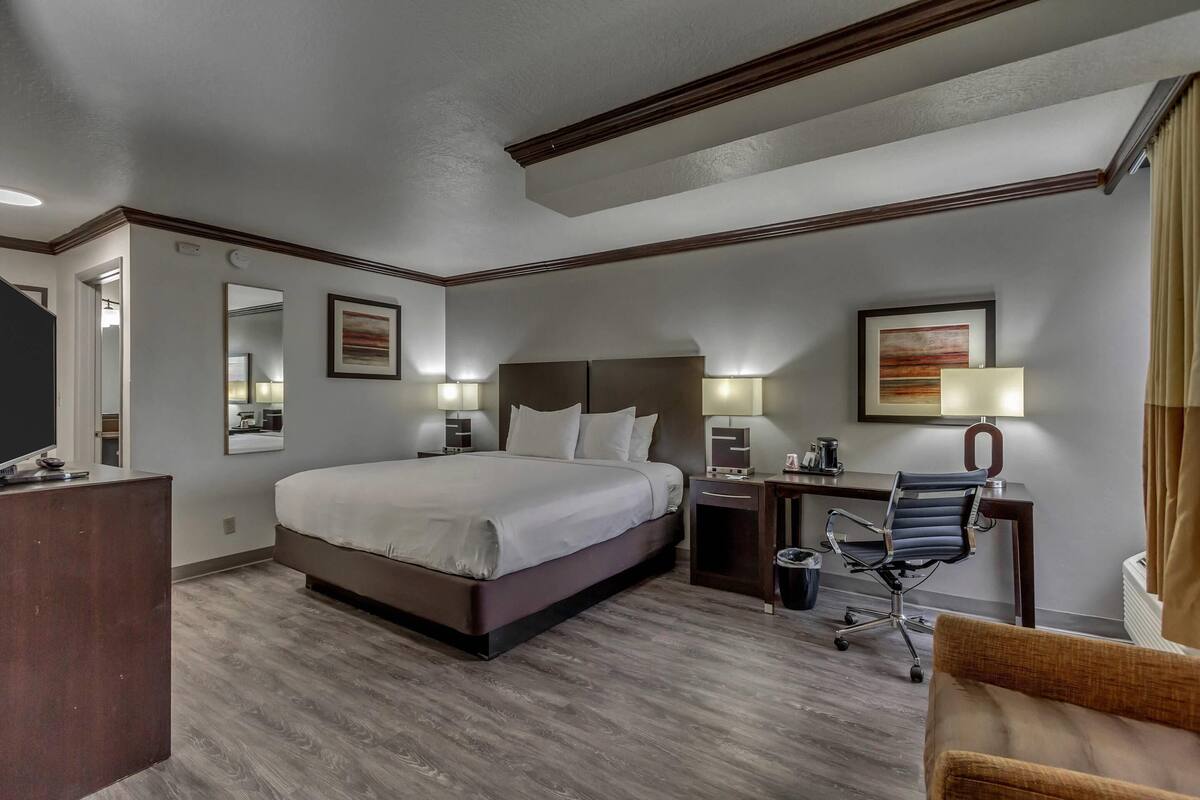 A hotel room with a large bed, a desk with a chair, a desk lamp, and a mirror.