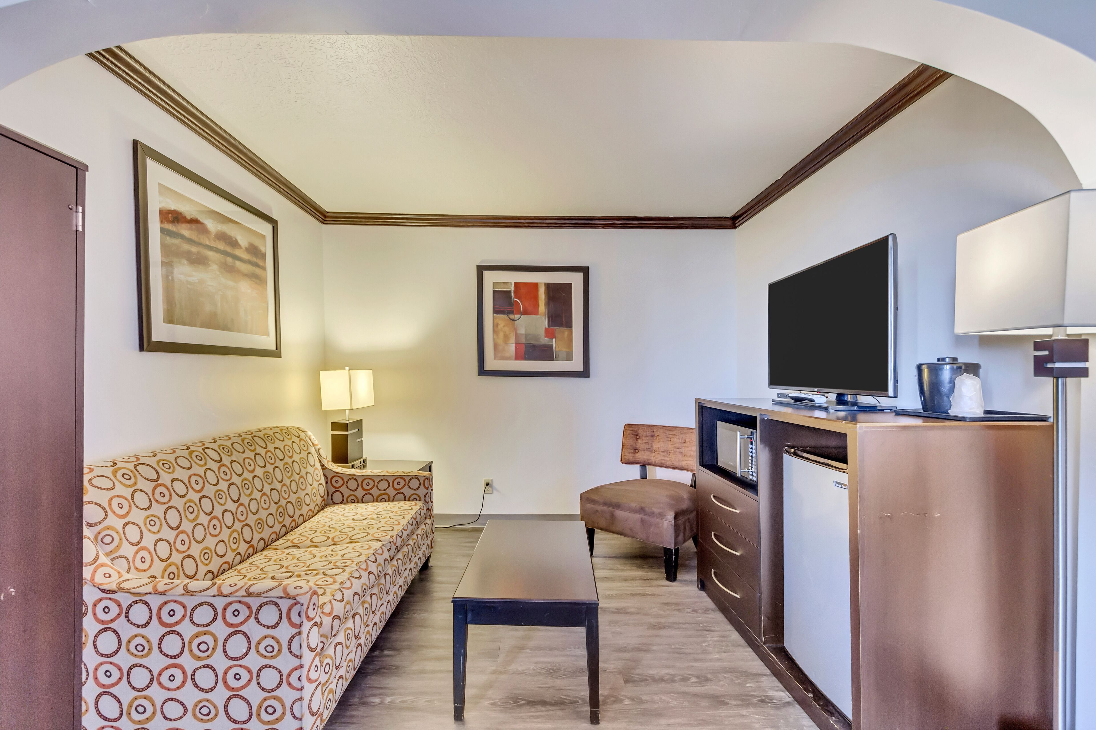 A compact hotel room with a sofa, a small table, a TV, a desk, and a cabinet.