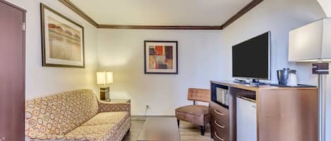 Una habitación de hotel compacta con sofá, una mesita, televisión, escritorio y armario.