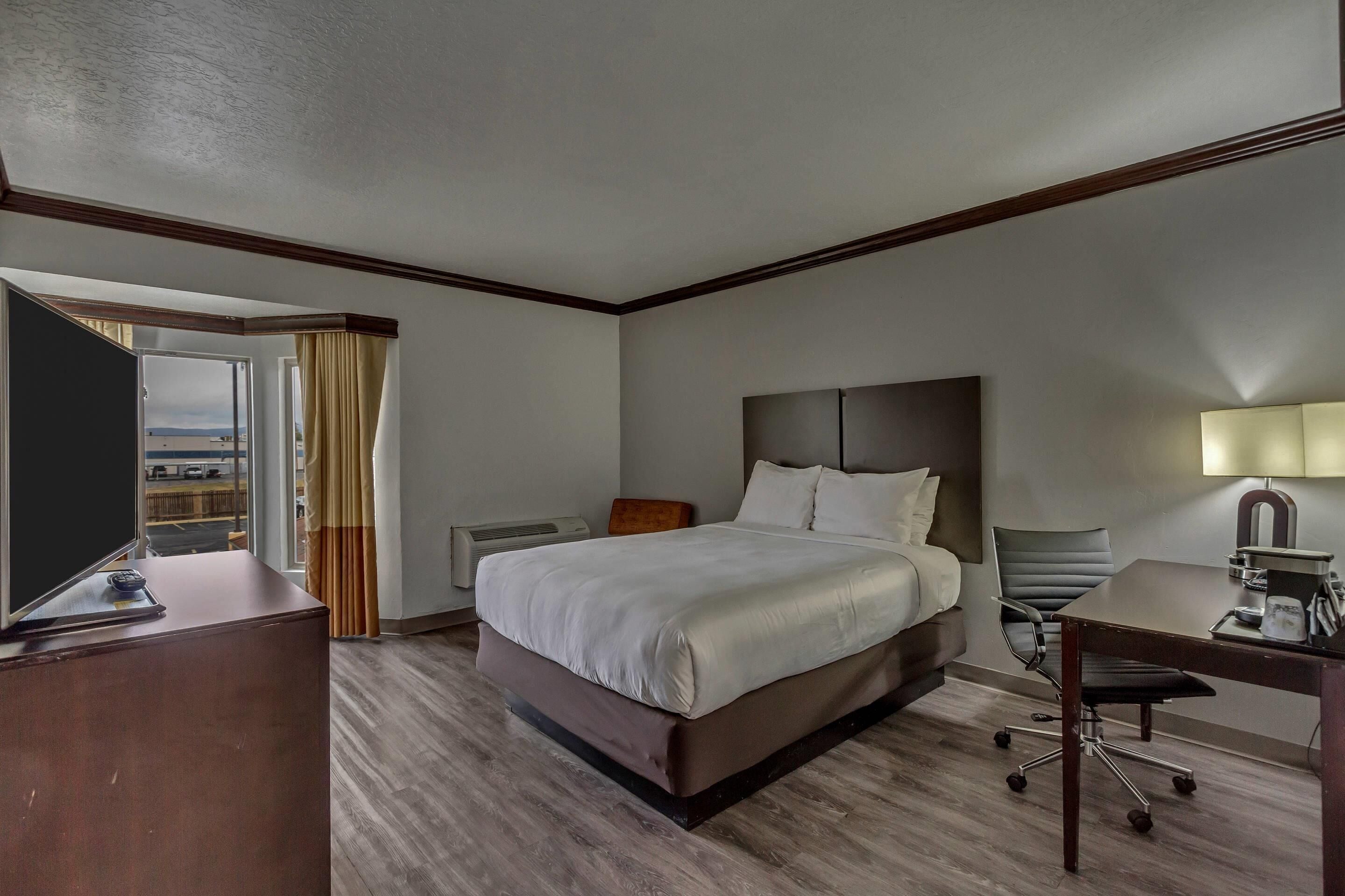 A hotel room with a large bed, a desk, a chair, and a TV.