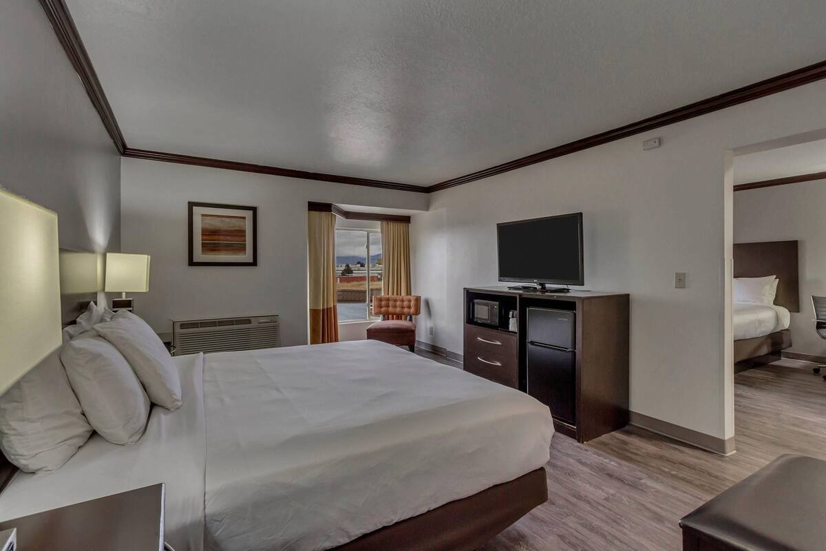 Ein Hotelzimmer mit einem großen Bett, einem Schreibtisch, einem Flachbildfernseher, einem Sessel und Blick ins Freie durch ein Fenster.