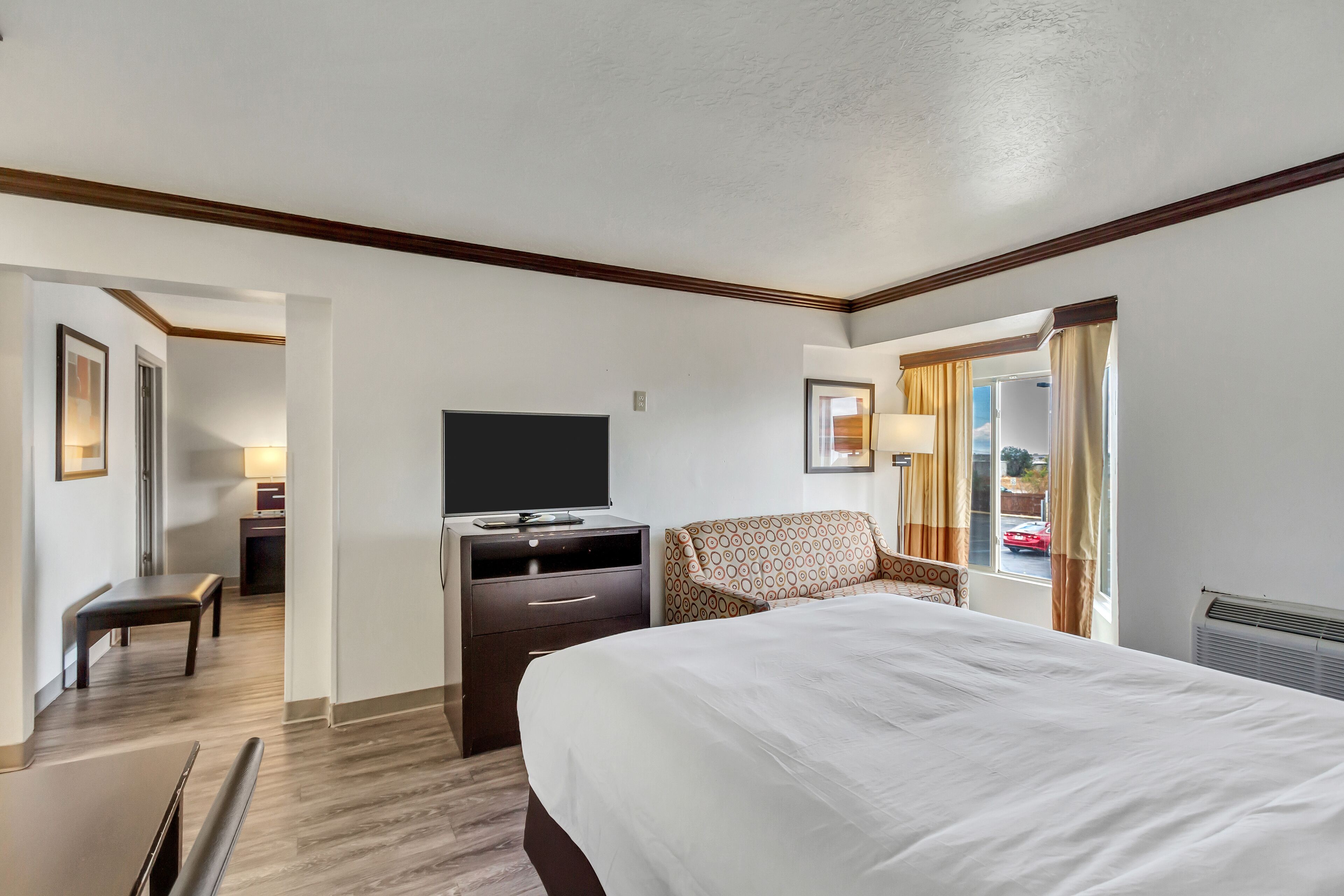 A hotel room with a large bed, a desk with a chair, a television, and a window with curtains.