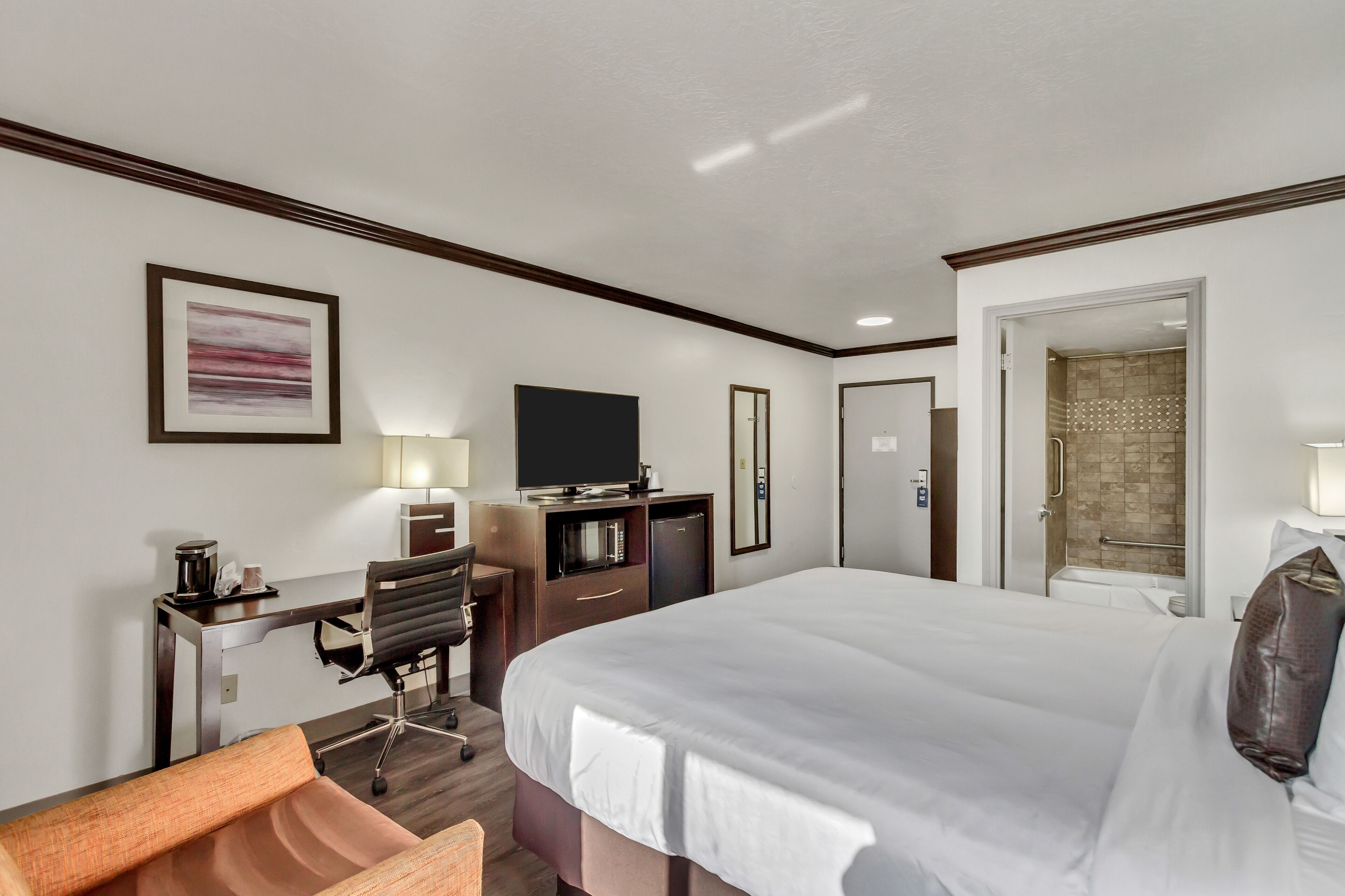 A hotel room with a large bed, a desk with a chair, a television, and a shower area.