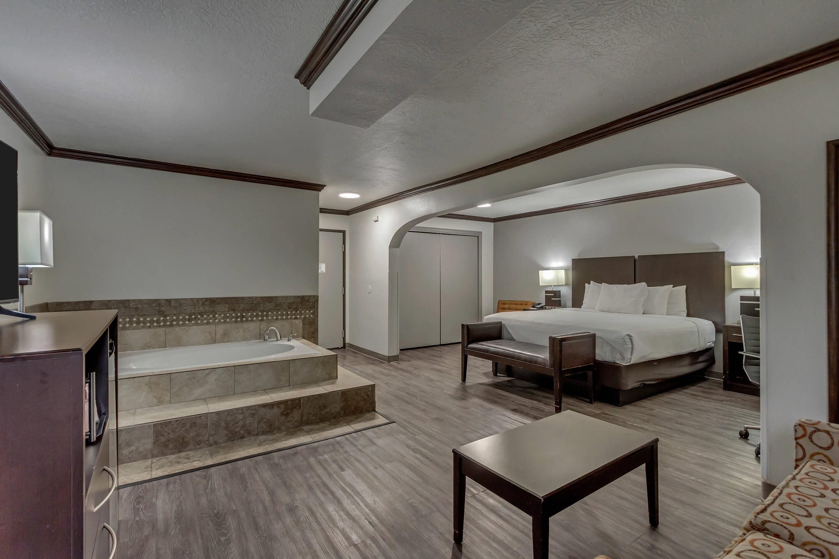 A hotel room with a bed, a desk, a chair, a sofa, a bathroom with a bathtub, and a staircase.