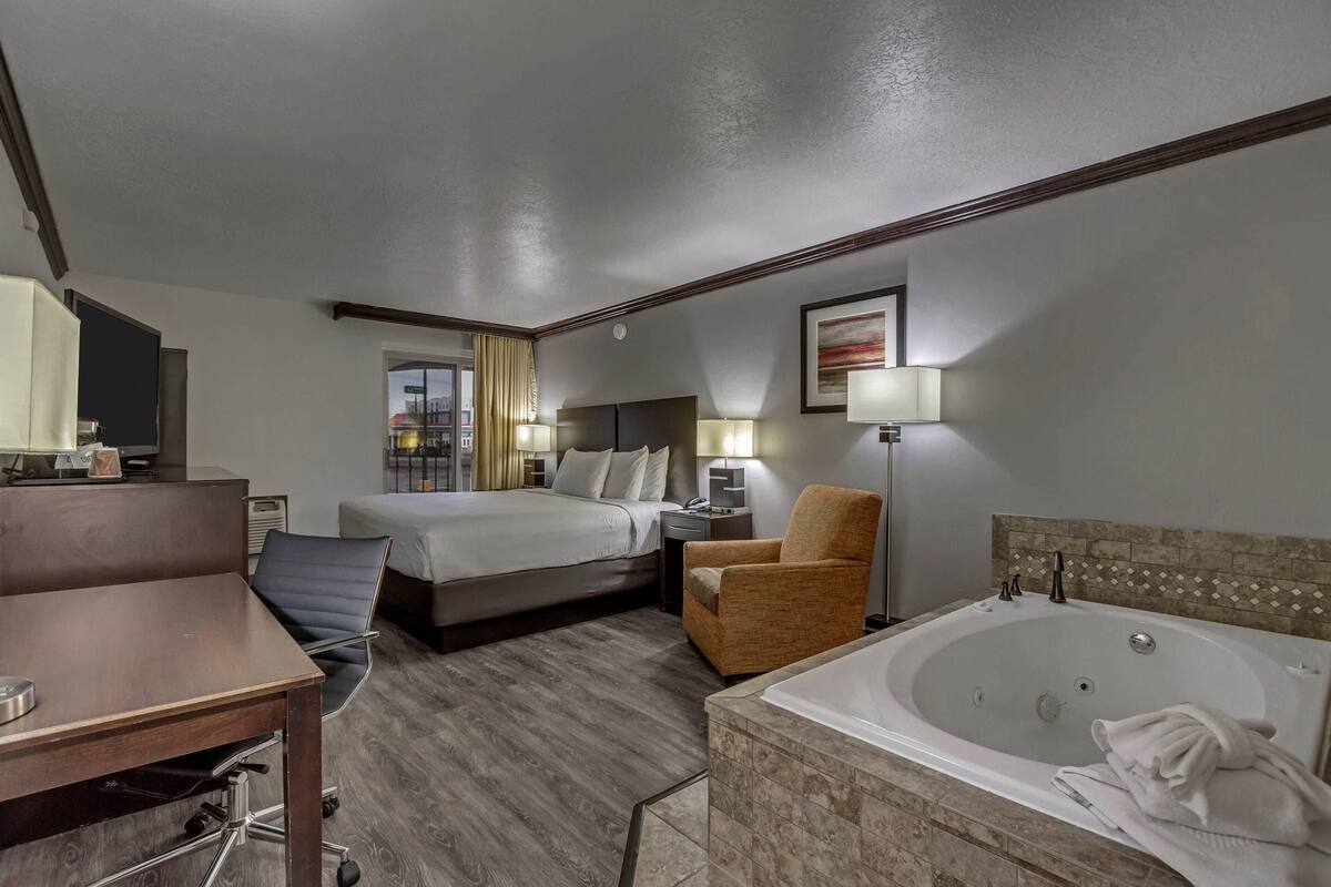Ein Hotelzimmer mit Bett, Schreibtisch, Stuhl, Schreibtischlampe, Nachttisch, Lampe und Badewanne.