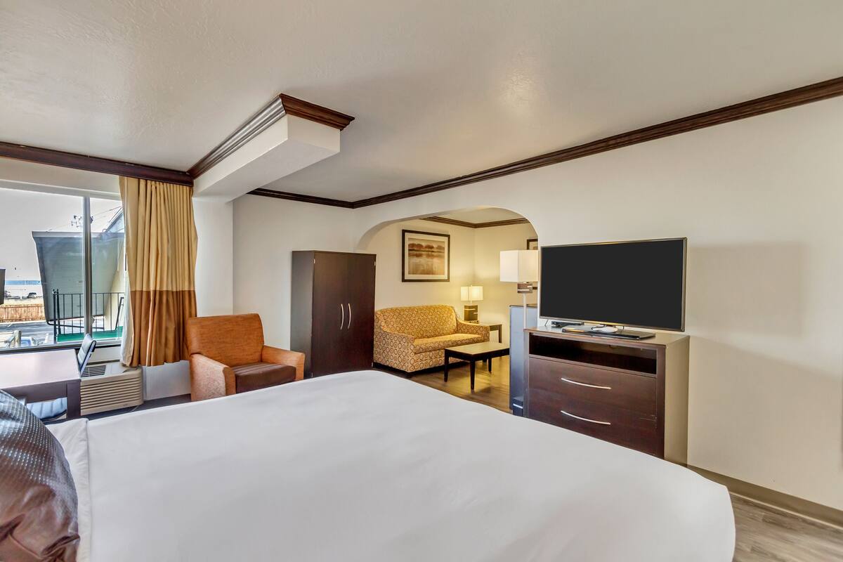 Ein Hotelzimmer mit einem großen Bett, einem Fernseher, einem Schreibtisch, einem Sessel und einer Sitzecke.