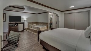 Habitación de hotel con una cama grande, un escritorio con televisor de pantalla plana, un baño con bañera y un vestidor.