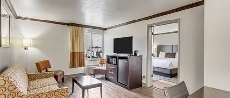 Ein Hotelzimmer mit einer Schlafcouch, einem Schreibtisch, einem Fernseher, einer Minibar und einem Bett.