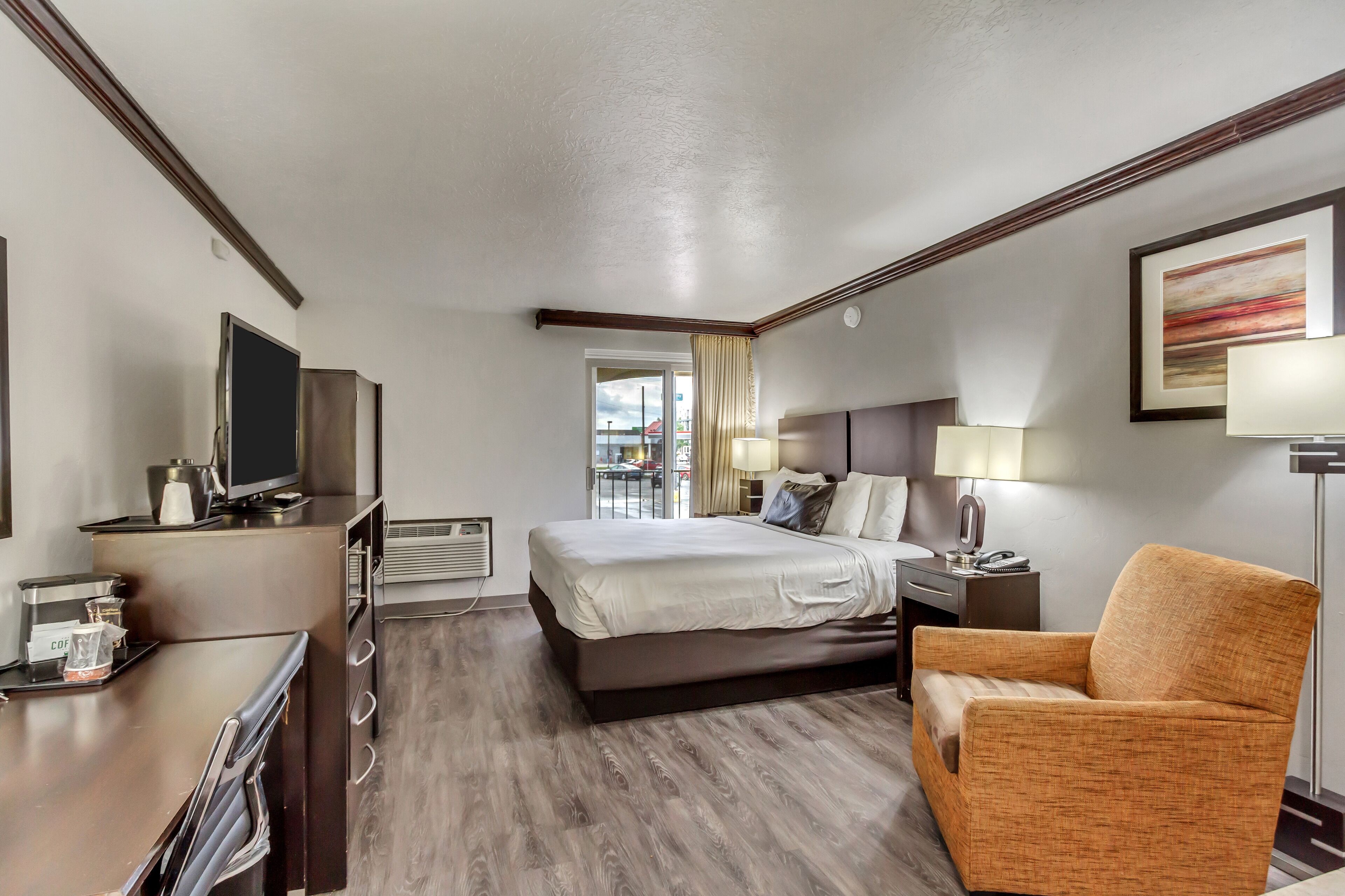 A hotel room with a bed, a desk with a coffee maker, a TV, and a chair.