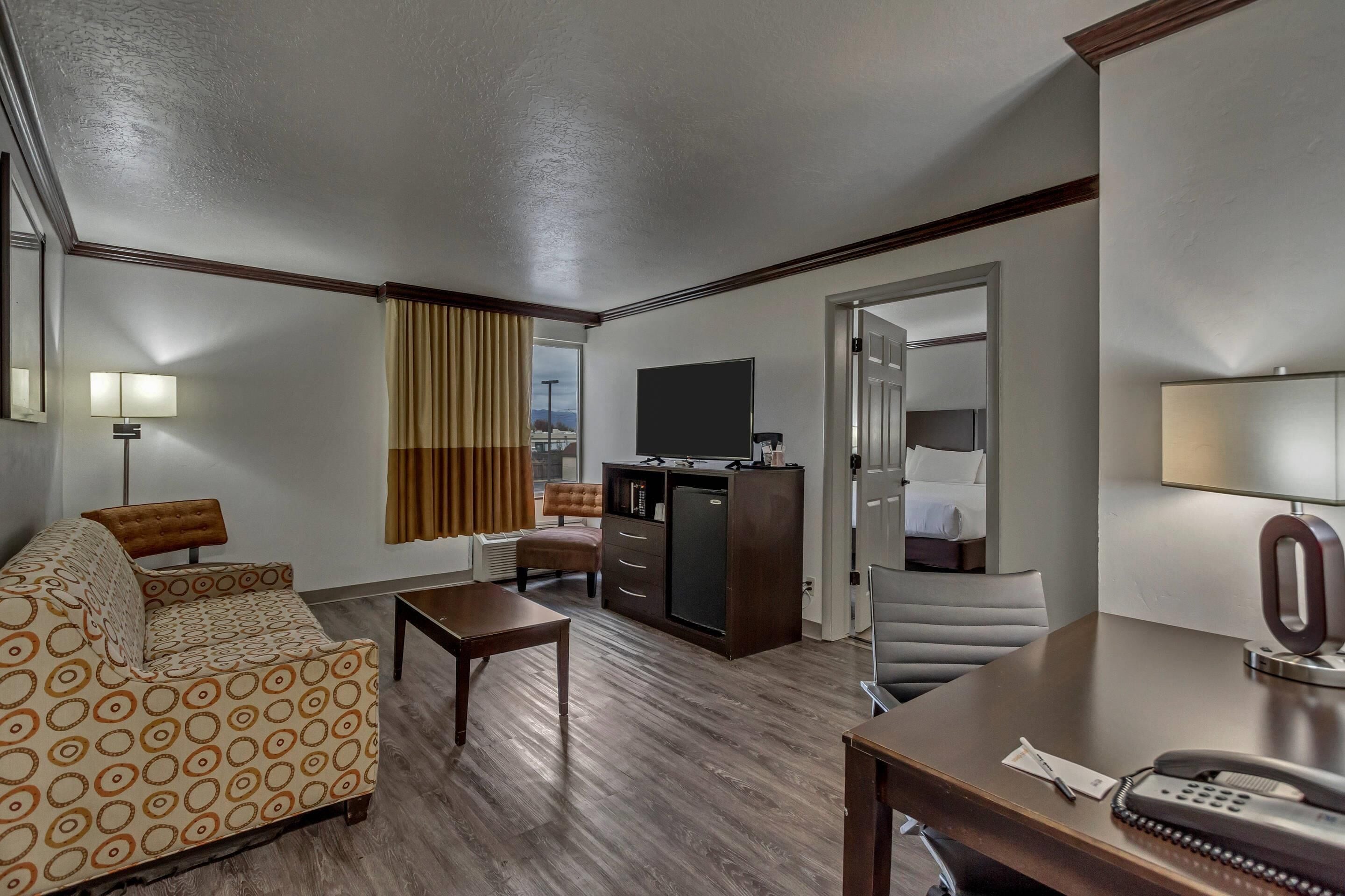 Ein Hotelzimmer mit Sofa, Schreibtisch, Stuhl, Fernseher, Minibar und Bett.