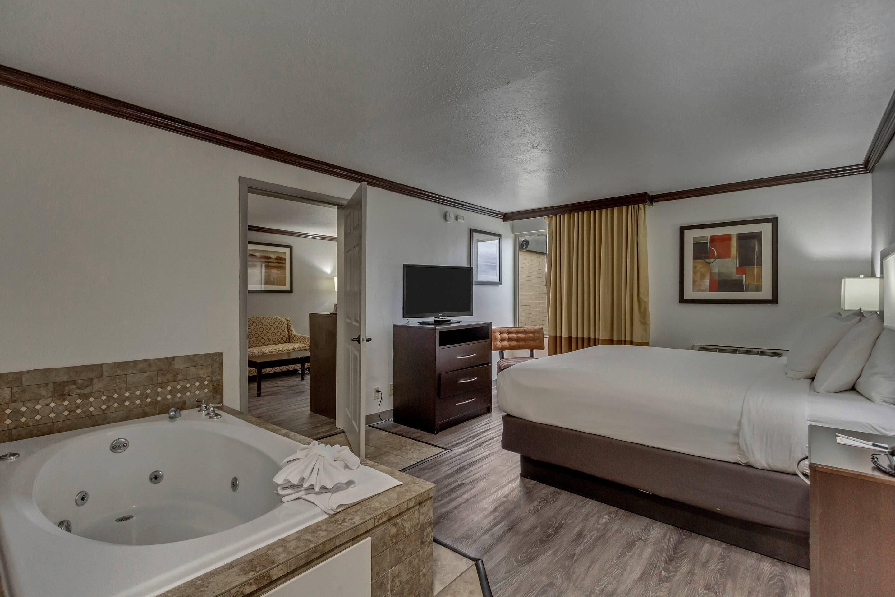 Ein Hotelzimmer mit einem großen Bett, einem separaten Badezimmer mit Badewanne, einem Fernseher und einem Schreibtisch mit Stuhl.