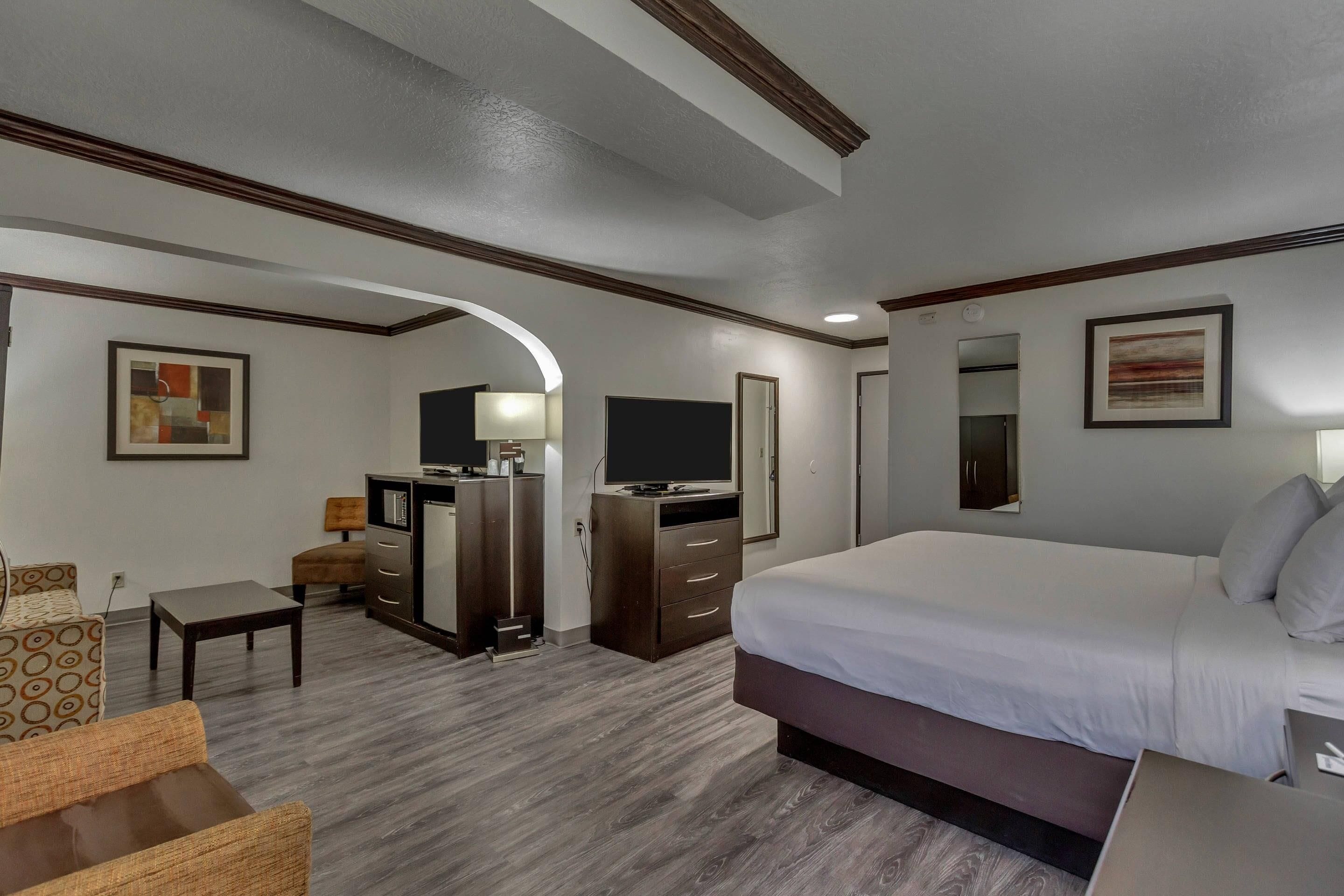 A hotel room with a bed, a desk, a chair, a dresser, a TV, and artwork on the walls.